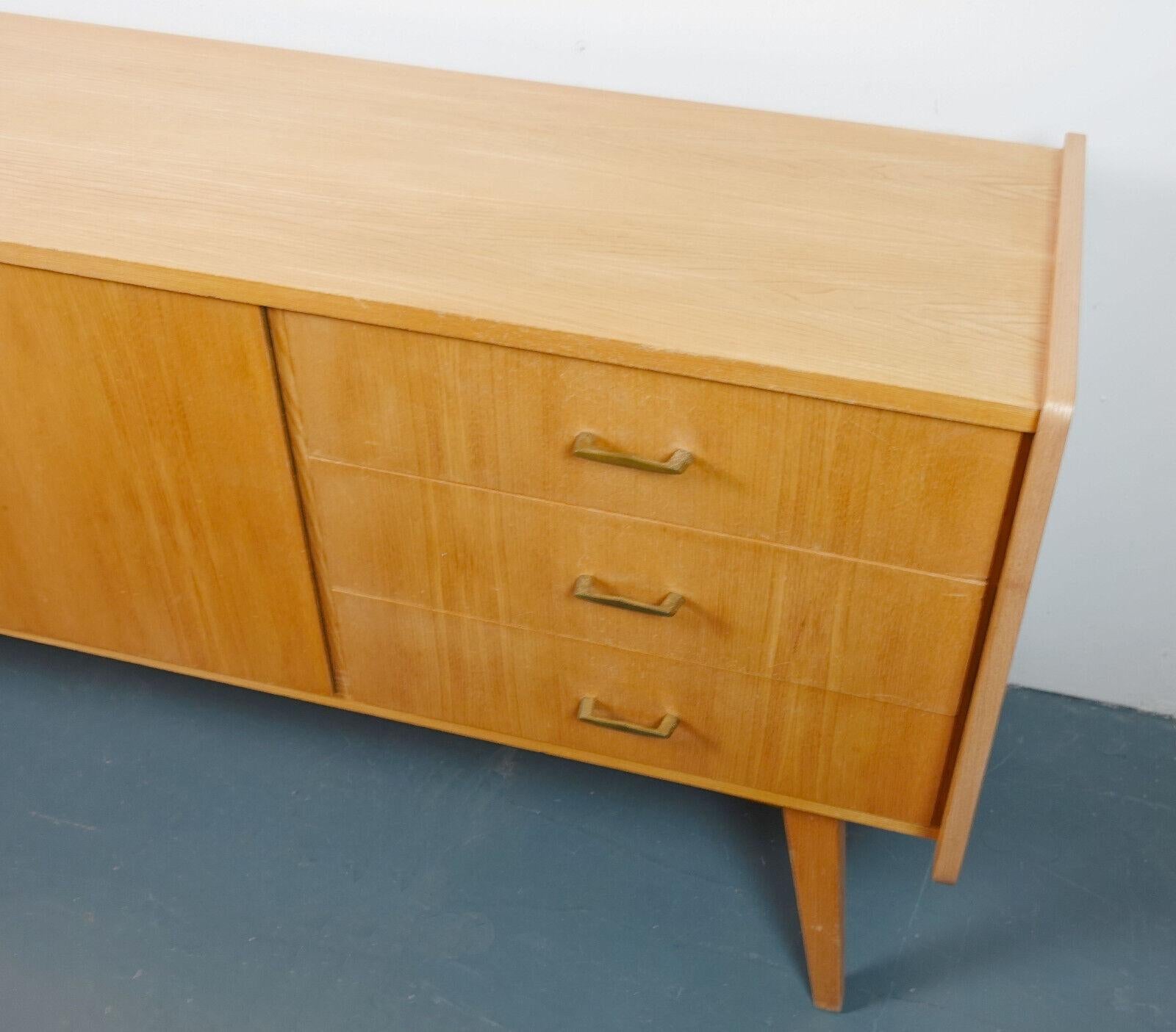 Elegant Mid Century Modern sideboard from the 50s, manufactured by Bartels-Werke. The body is completely coated with Rüster real wood veneer, the interior is veneered with mahogany. The sideboard stands on slanted legs.
On the left is a double door