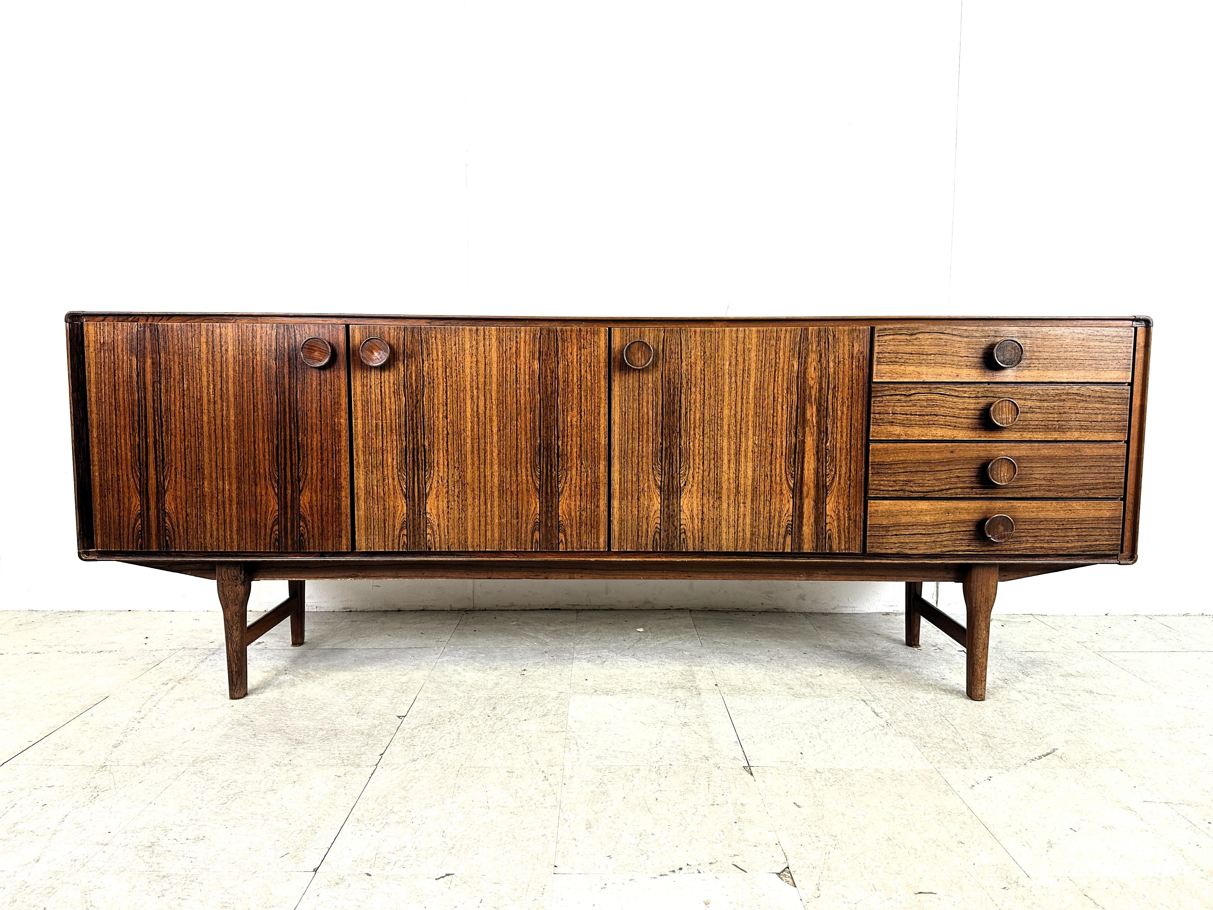 Gorgeous mid century sideboard model FDT-1205 by Fristho Franeker with beautiful natural wood veining. 

The sideboard has 3 doors and 4 drawers each with a beautifully crafted handle.

The legs also have an elegant design to them.

Good overall