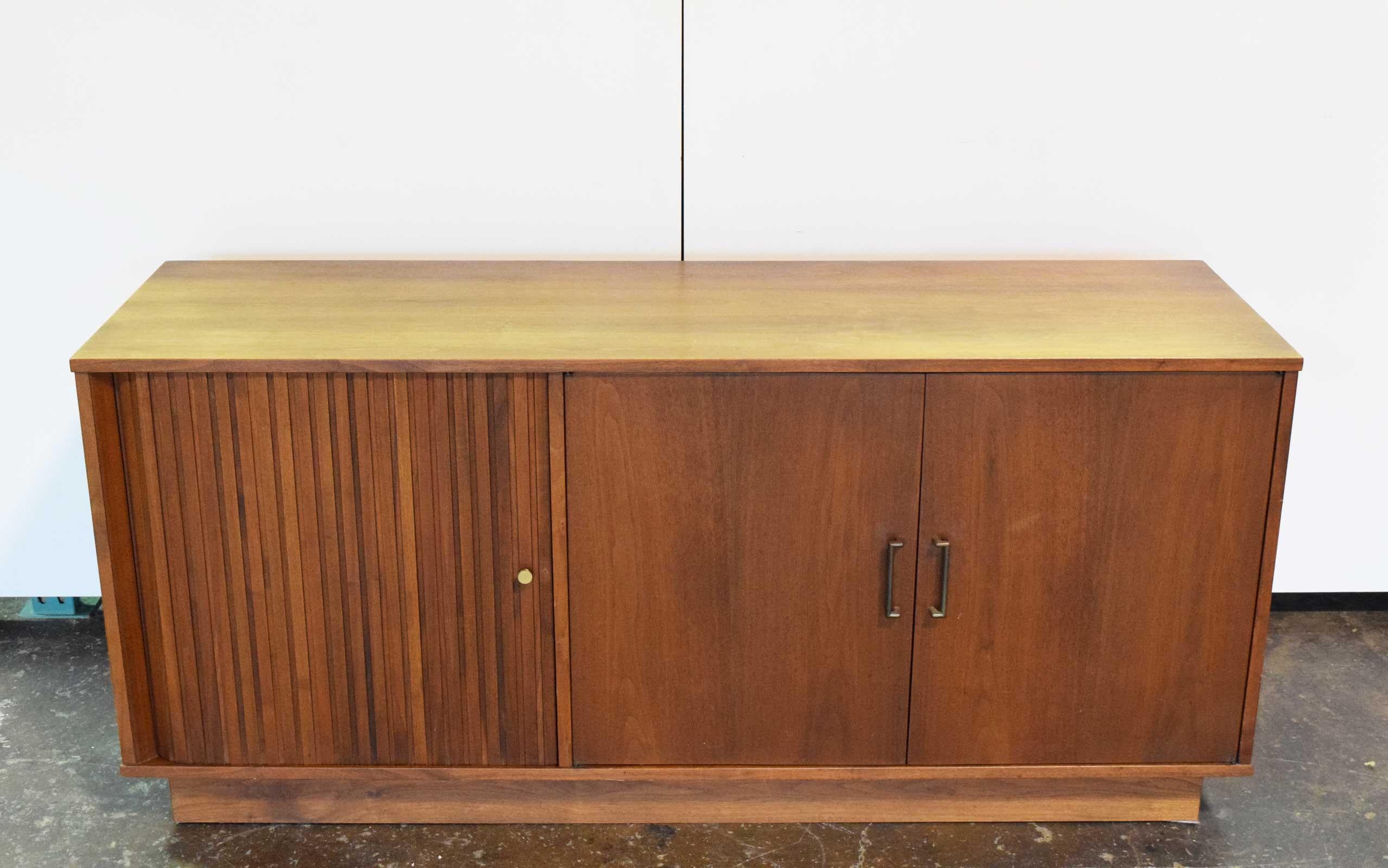 Sideboard has tambour door on one side with a shelf for TV and other side has shelving. Brass handles.