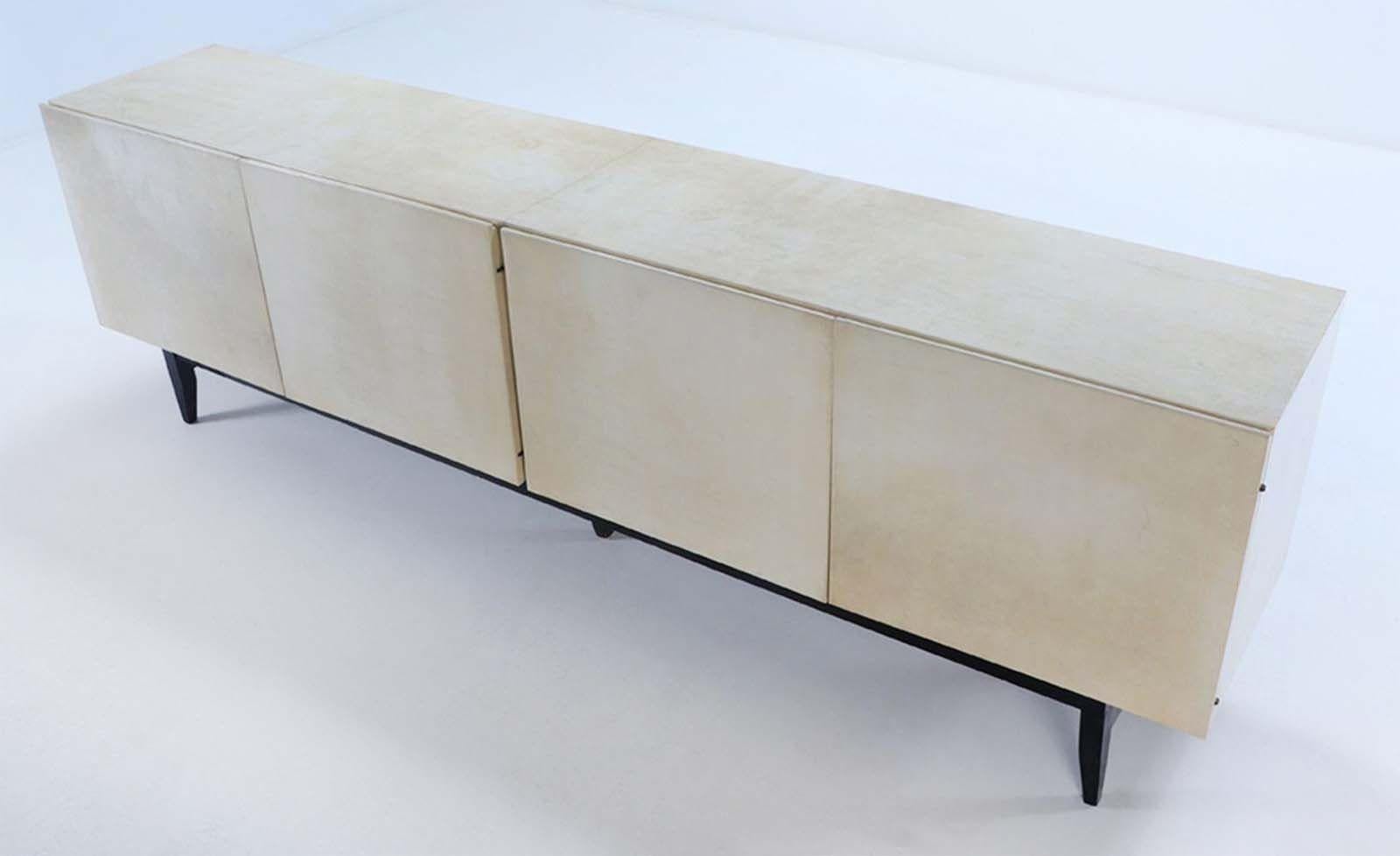 Sleek mid-century sideboard in neutral tone in the style of Karl Springer. Its sleek design features a lustrous parchment exterior, accentuated by an ebonized wooden base that adds a touch of richness to its overall aesthetic.
Boasting four spacious