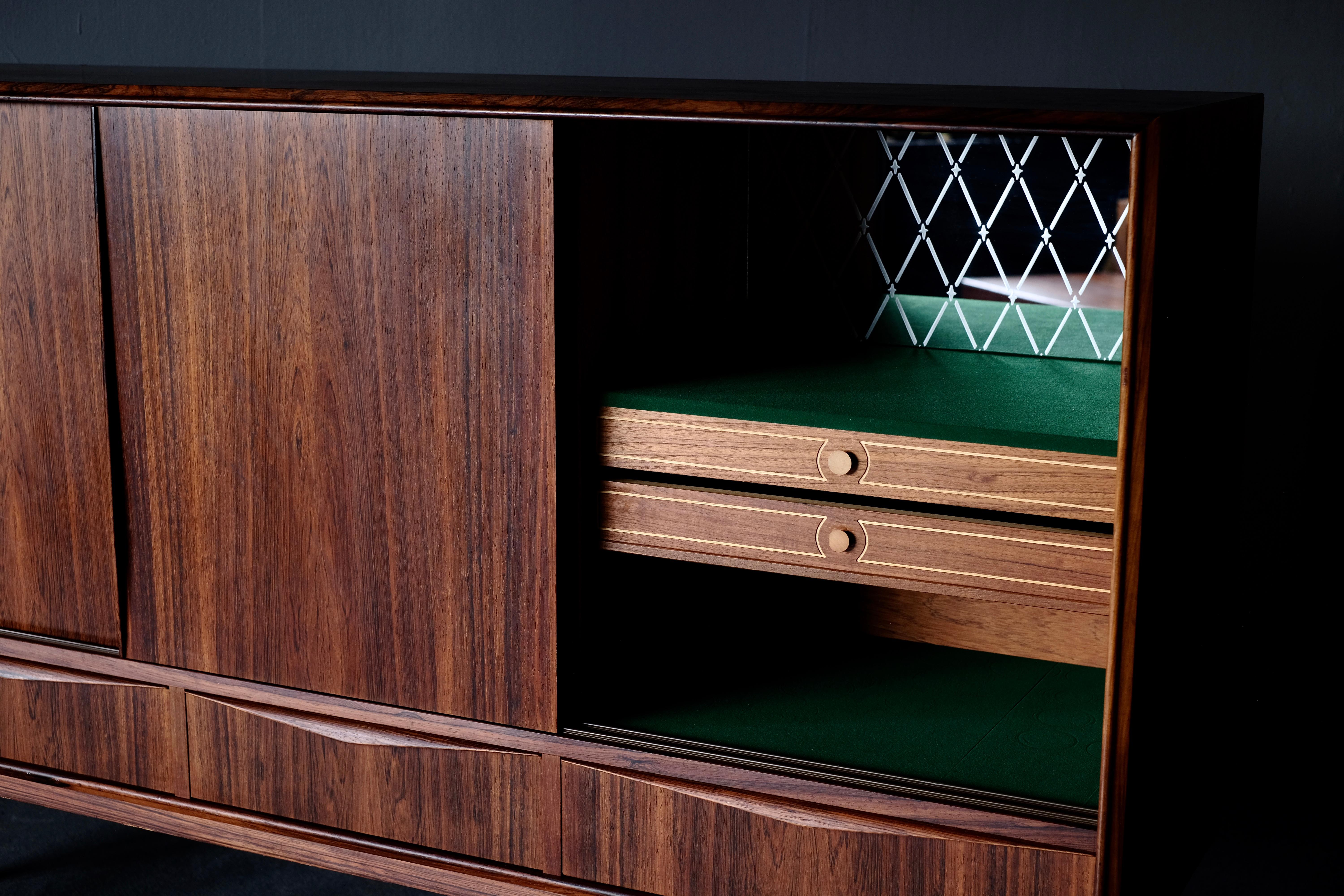 Sideboard in rosewood. It has front sliding doors and 4 drawers. The sliding doors open to house felt lined drawers and shelves. The details like the tapered legs and the elegant drawer pulls are distinctive in 1960s pieces such as this.