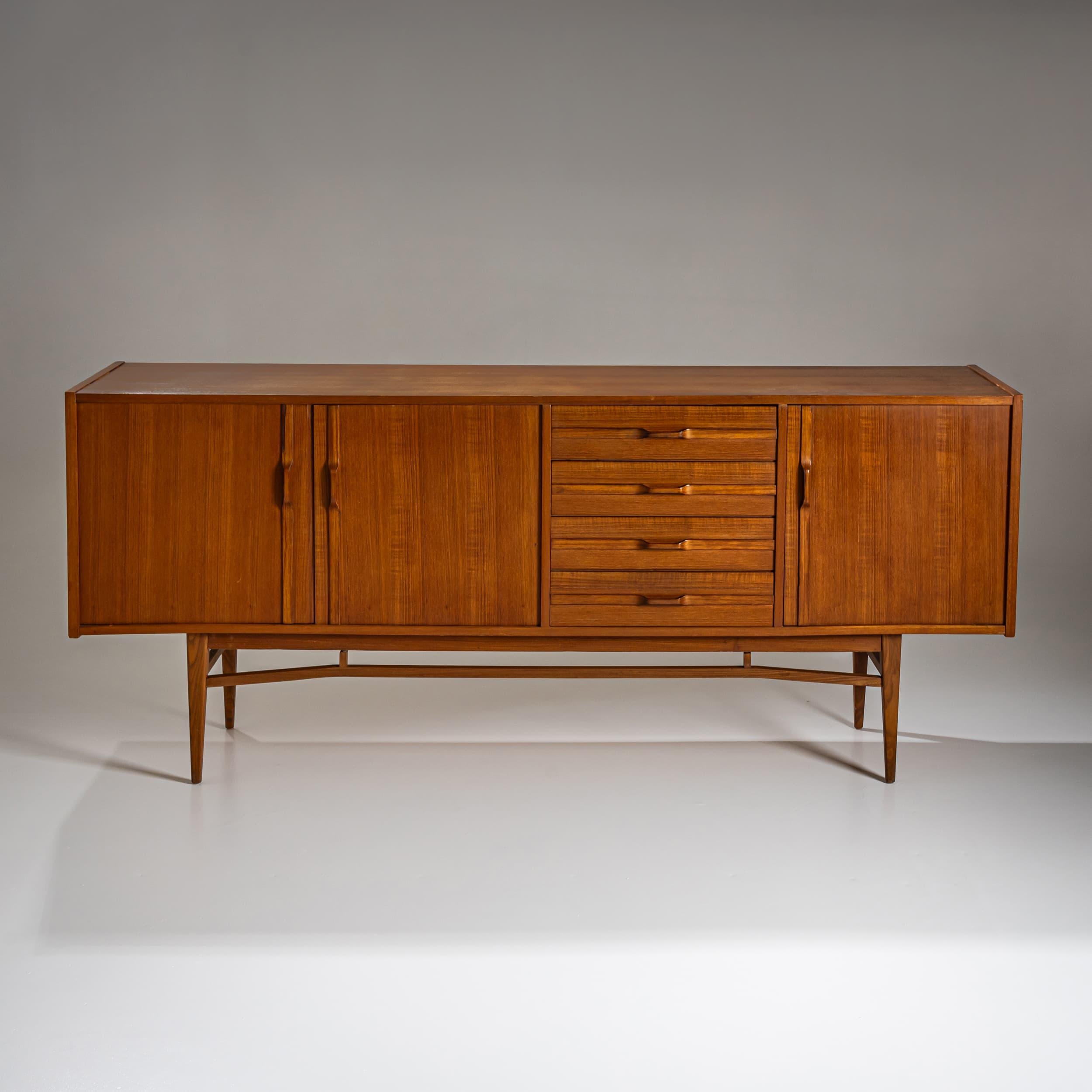 Geräumiges Sideboard aus der Mitte des Jahrhunderts, wahrscheinlich italienischer Herkunft, aus den 1960er Jahren. Der Korpus ist mit warmtonigem Teakholzfurnier verkleidet und verfügt über drei Türen und vier eingelassene Schubladen. Es ruht auf