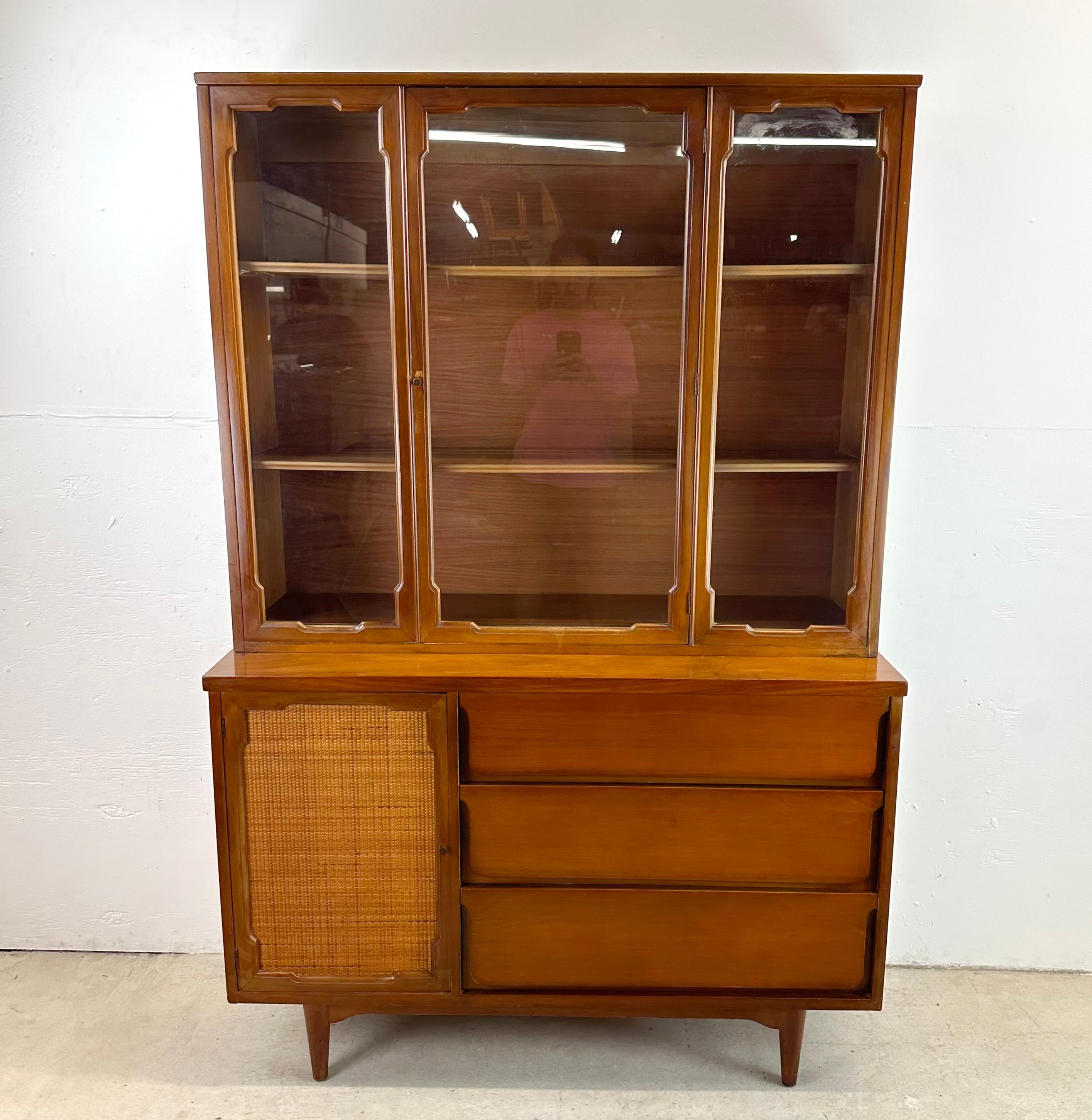 This mid-century Walnut china cabinet features unique vintage design in the style of the esteemed designer Jack Cartwright. This exquisite piece seamlessly fuses classic design with functional craftsmanship, making it a captivating addition to any