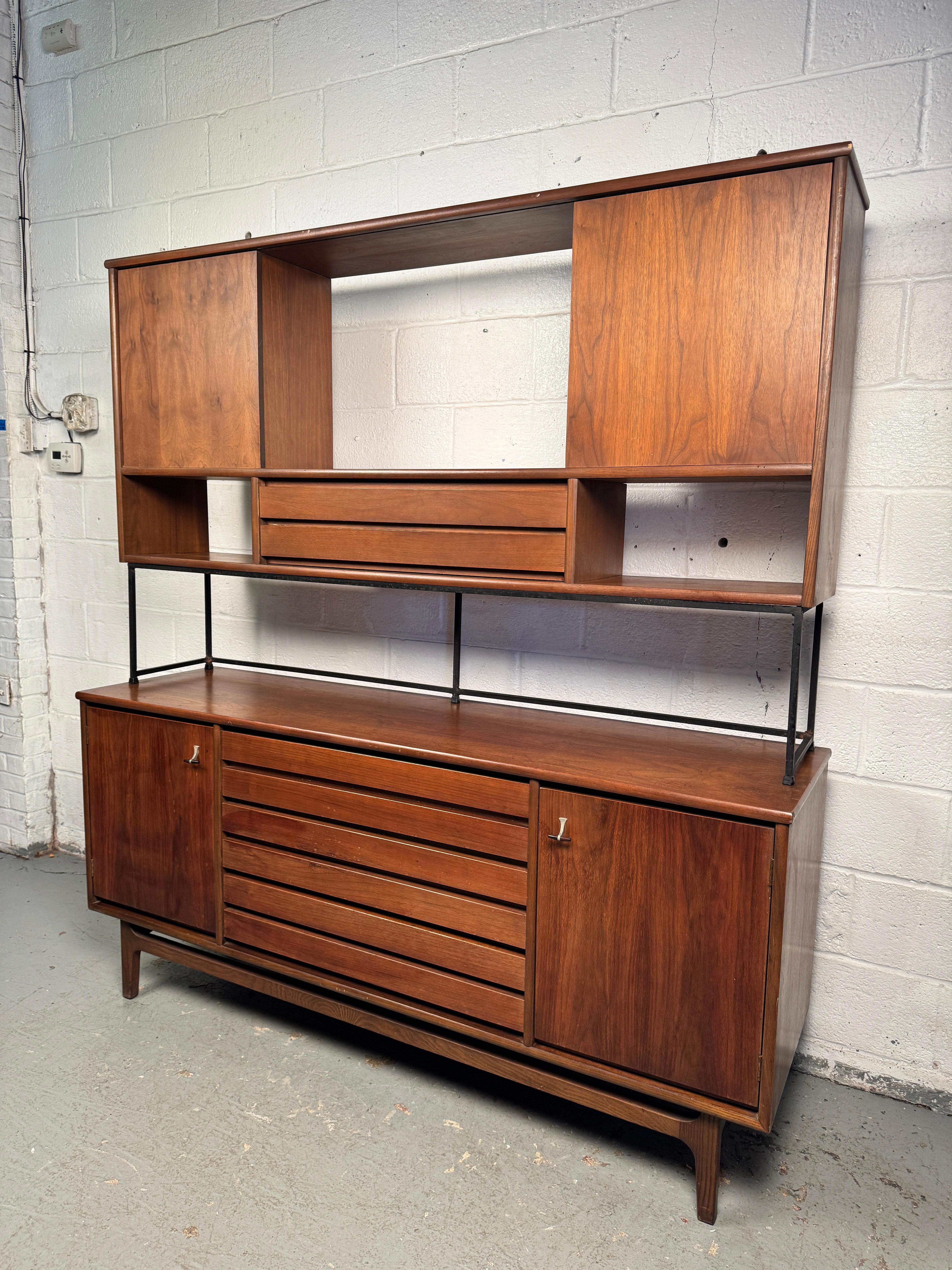 Distinctive sideboard manufactured by Stanley, featuring a sleek mid-century profile with an attached upper cabinet topper. Crafted in fine wood with clean lines and ample storage, this piece combines functionality with bold design, making it a