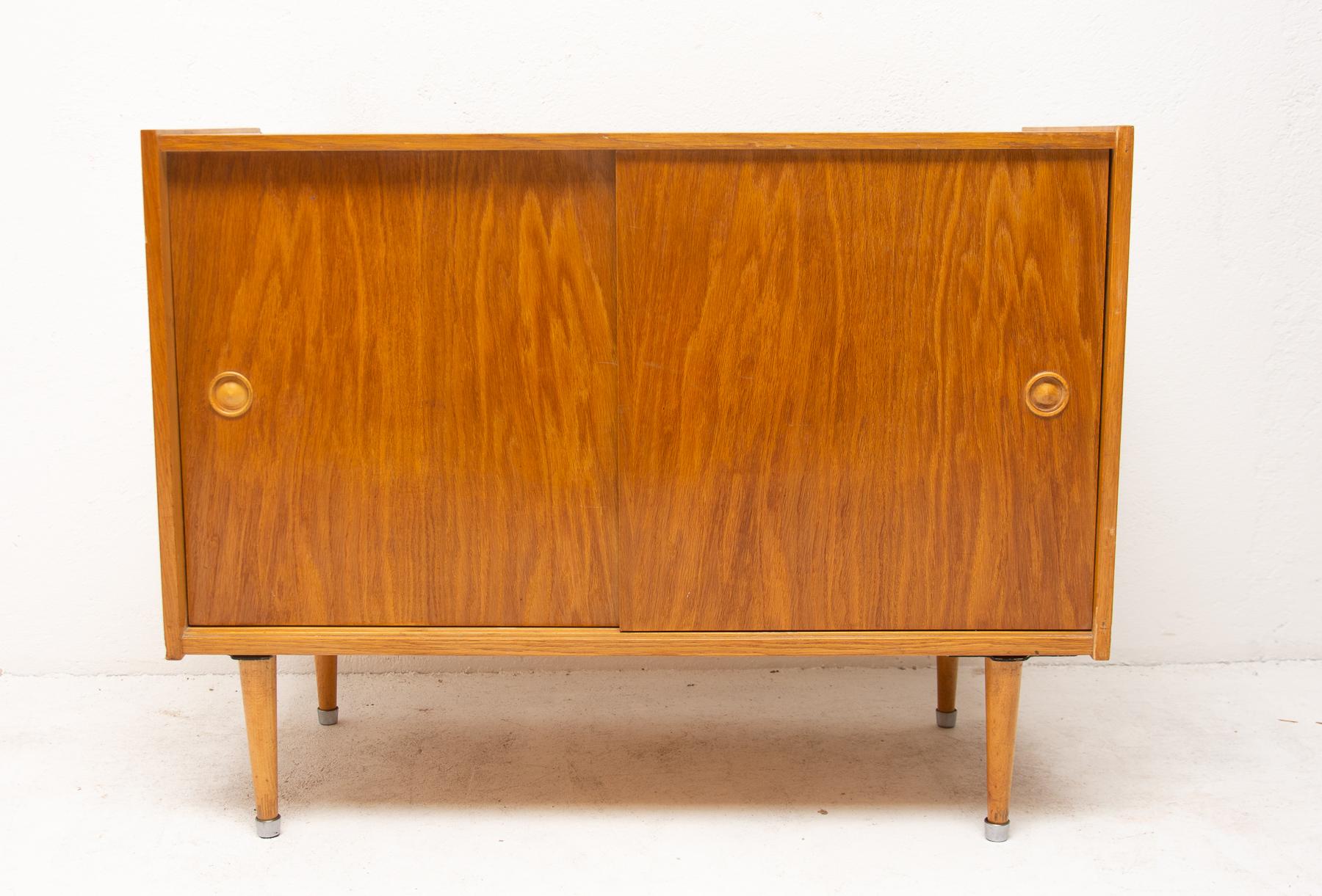 Midcentury sideboard or chest of drawers. It features a sliding doors. It´s made of wood and plywood, veneered in a polished oak wood. It was produced by Zapadoslovenske Nabytkarske Zavody, a furniture company in Czechoslovakia in 1960s. In very