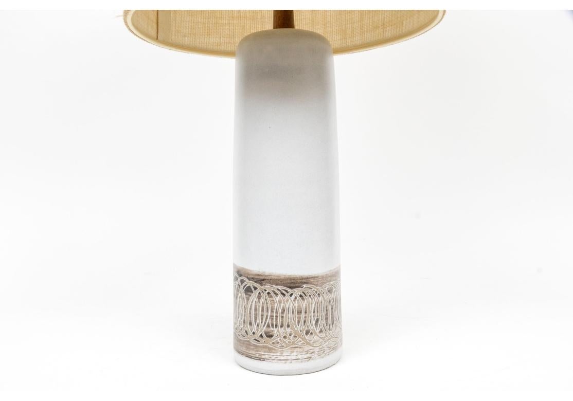 A Classic Mid Century Pottery base lamp circa 1960's. By Jane and Gordon Martz. A whit cylindrical lamp with a wide gray scrolled band at the base. With a wood topper support and finial. With a fabric drum shade.

Dimensions: 29 1/2