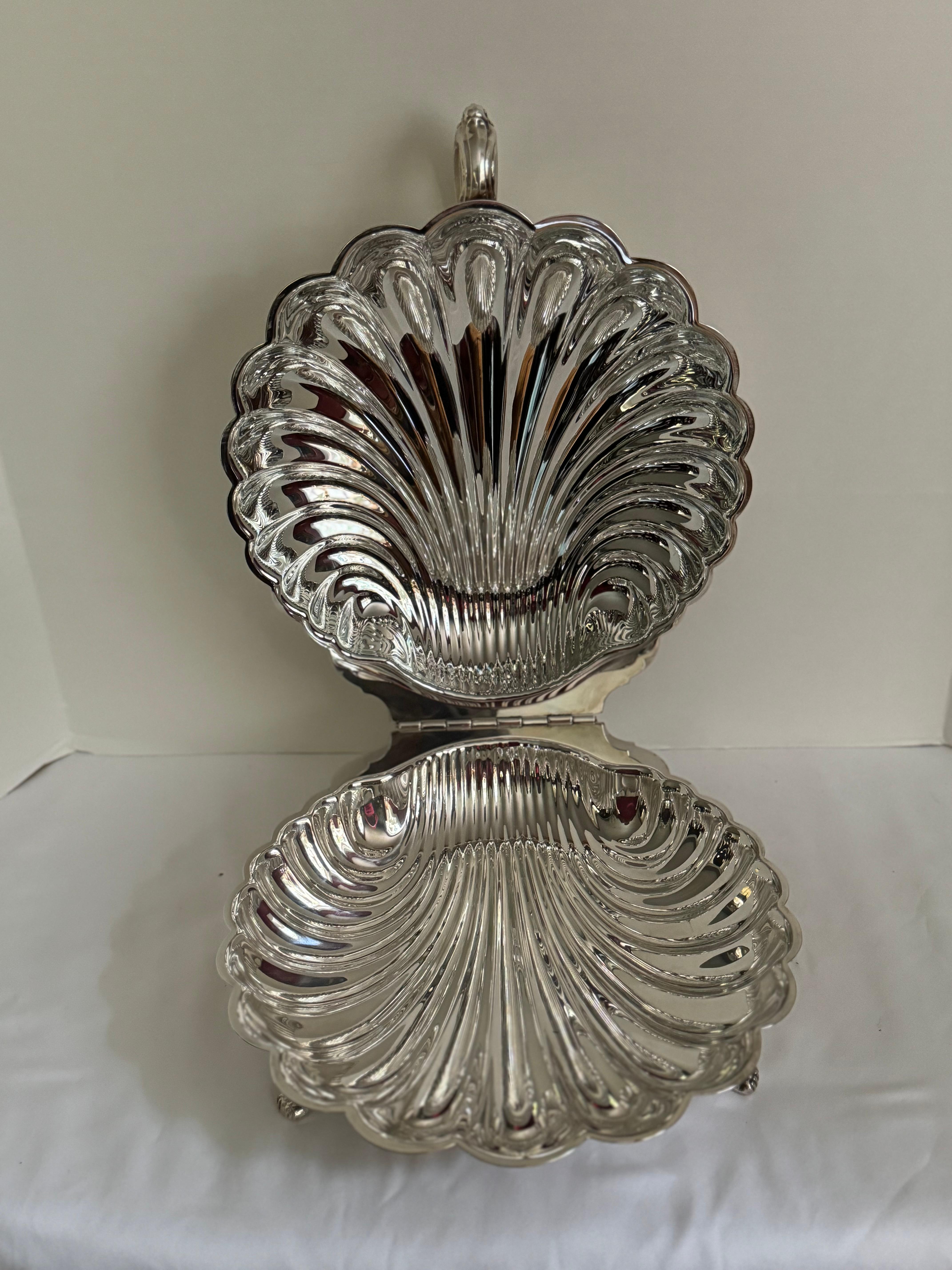 Vintage Silver Plate Serving Shell Dish, magnifique coquille de service surdimensionnée en métal argenté.  Il s'ouvre sur une charnière et repose sur des pieds décoratifs à griffes. Le dessus est orné d'un motif floral décoratif.  poignée détaillée 