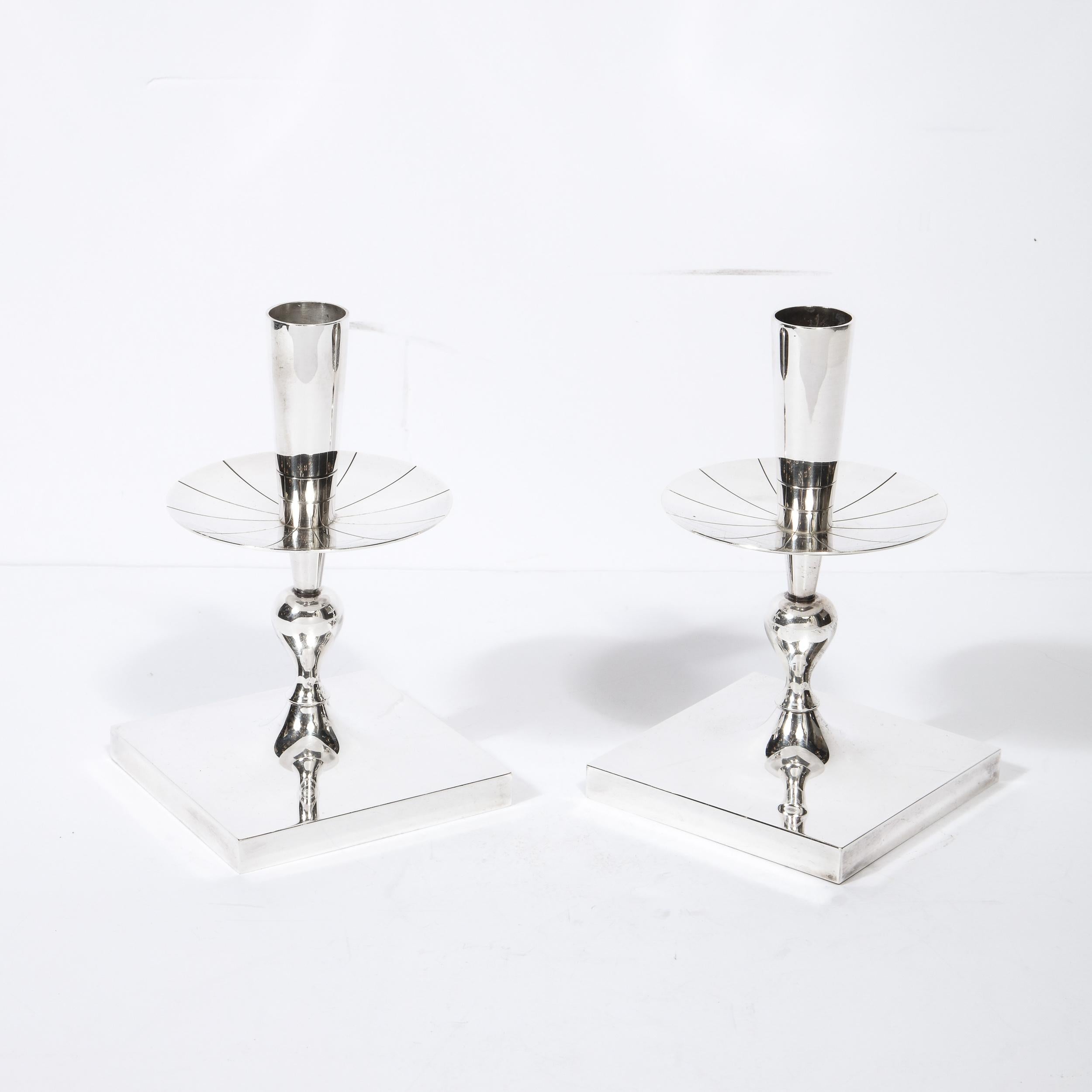 This gorgeous pair of silver plated candlesticks were designed by Tommi Parzinger for Dorlyn Silversmiths in the United States circa 1950. They feature volumetric square bases; sculptural undulating bodies; and circular striated bobeches- all in