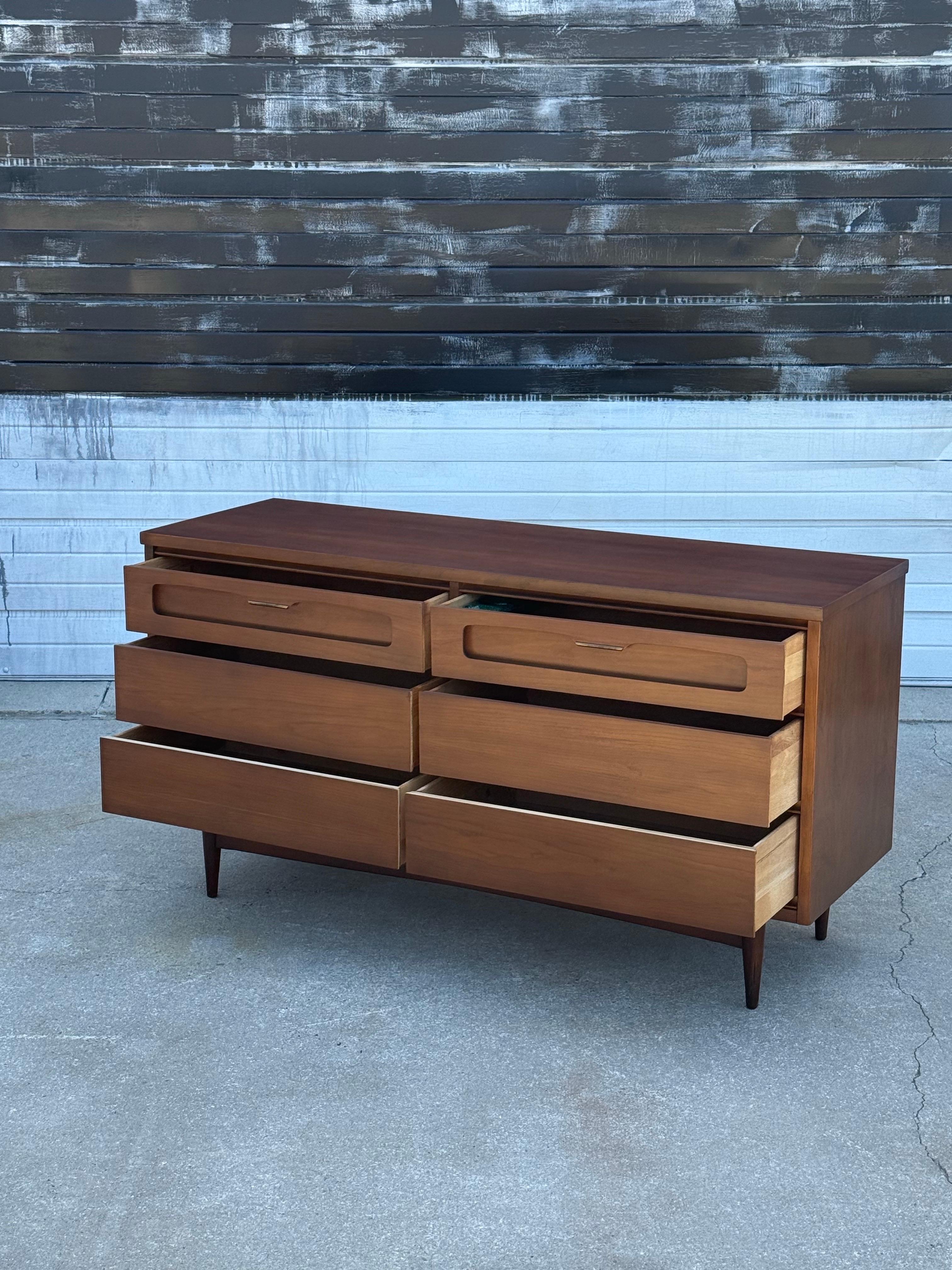 Mid century petite 6 drawer walnut dresser by Bassett. Very cool stretcher base with two brass finish top drawer pulls add nice detail to this dresser. All drawers function well. Very minor patina and minimal wear. We have polished the sides, fronts