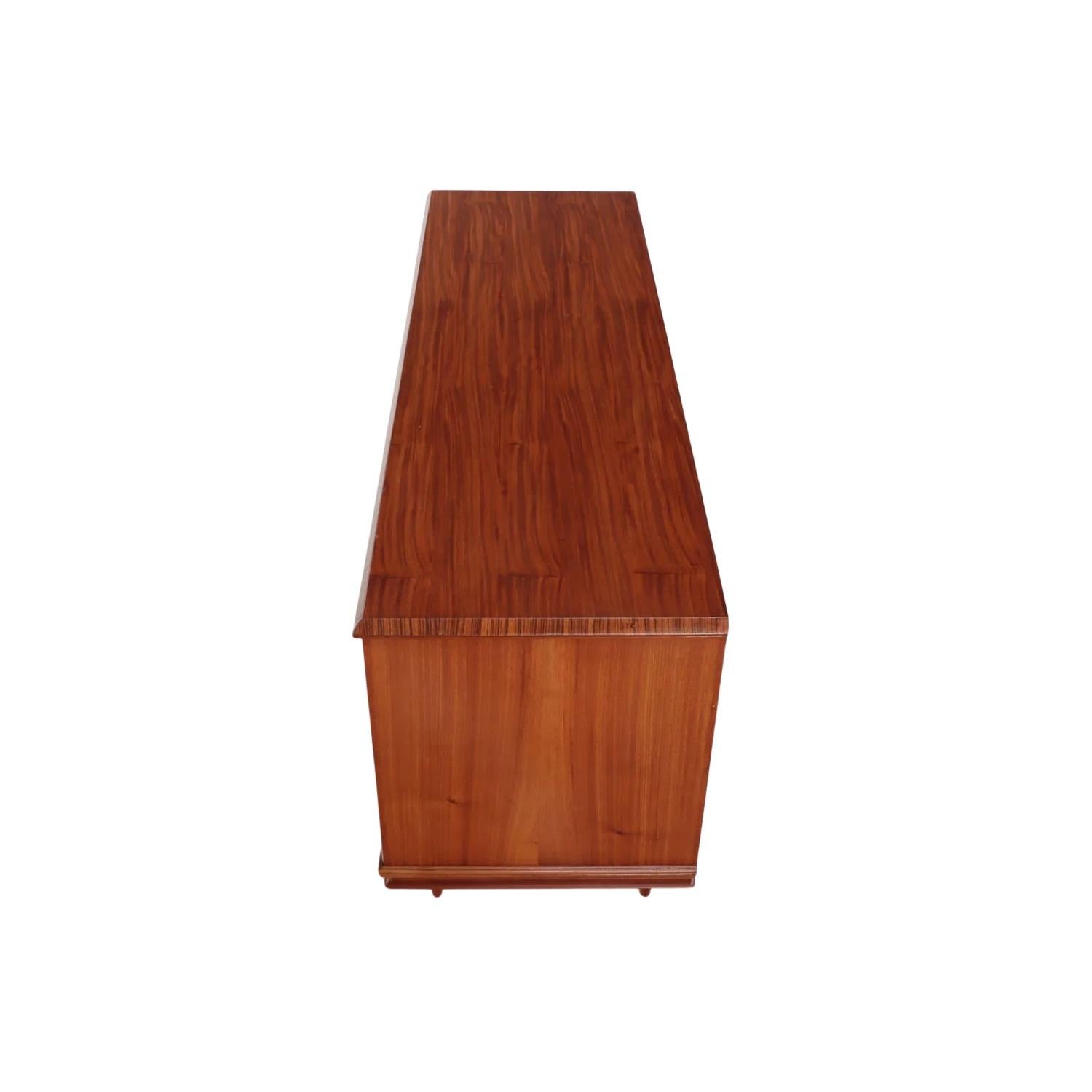 Comò a sei cassetti di metà secolo con ferramenta in ottone e gambe tornite. Il pannello decorativo verticale al centro del pezzo indica un alto livello di artigianato e design. Inoltre, questo pezzo è caratterizzato da un'importante figurazione sia