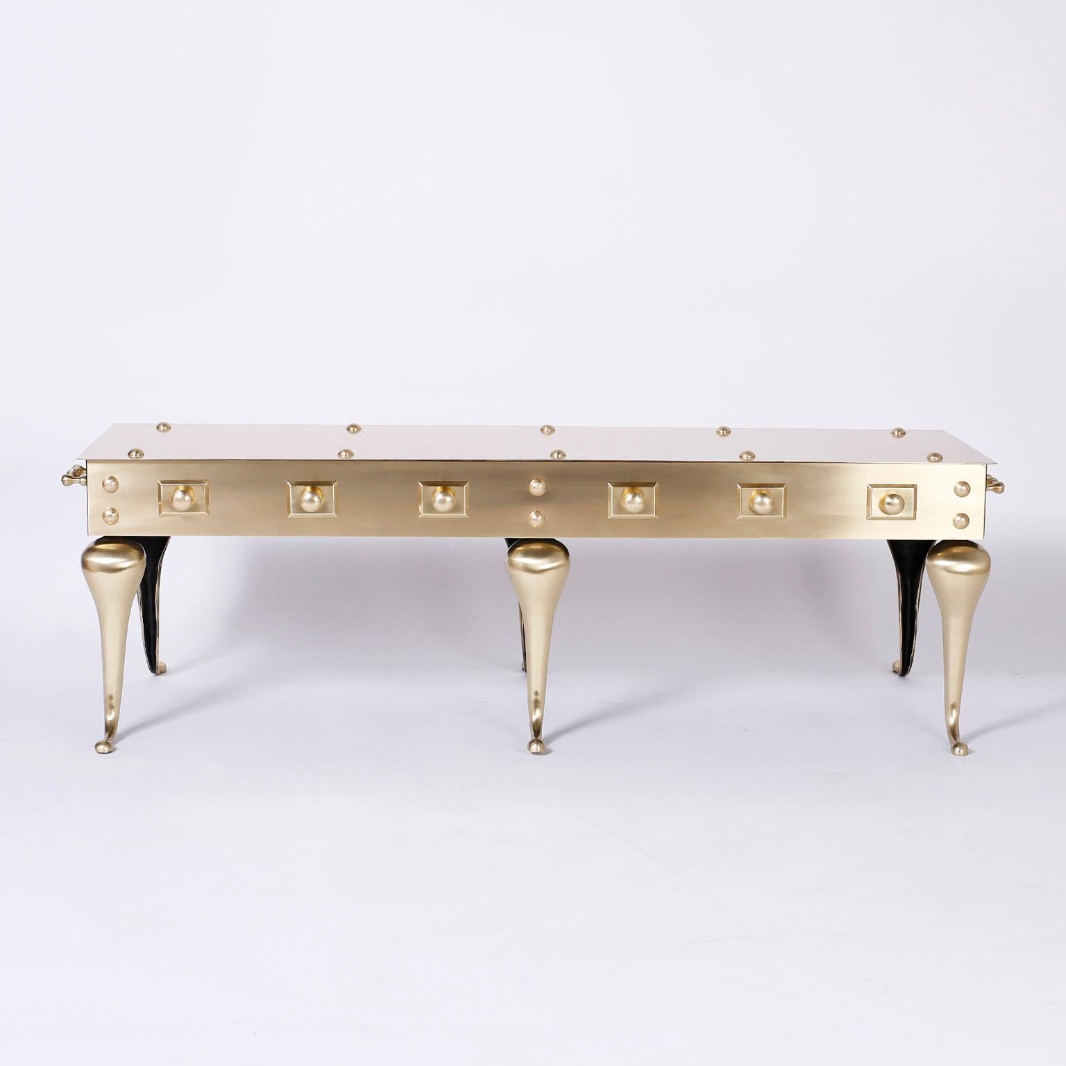 Exciting brass coffee table that is a hip midcentury version of a Queen Anne hearth stand with six distinctive legs, side handles, and decorative faux rivets. Hand polished and lacquered for easy care.