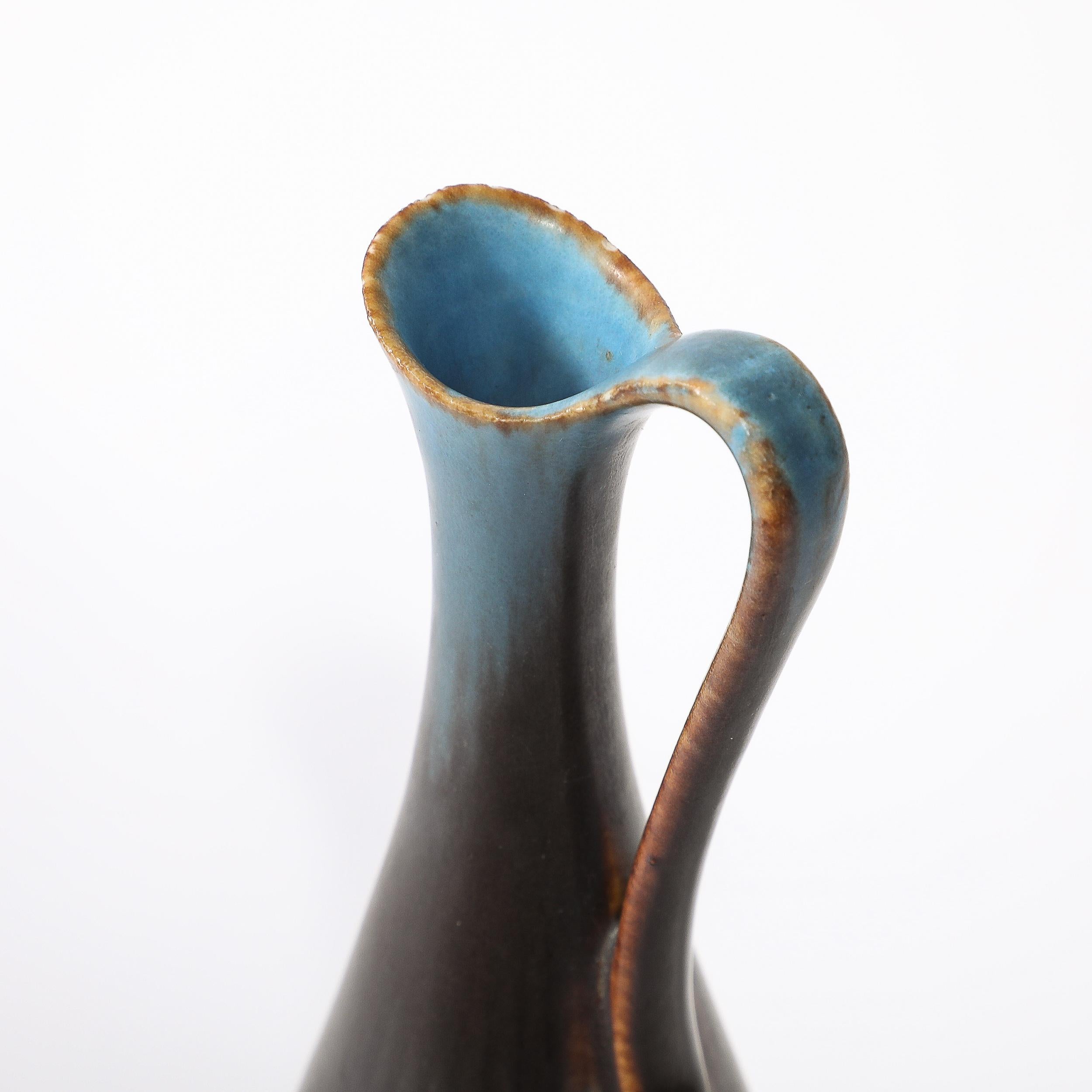 Diese schöne himmelblaue & kupferne Kanne/Vase von Gunnar Nylund für Rörstrand stammt aus Schweden, CIRCA 1950. Diese Vase zeichnet sich durch ein elegant geschwungenes Profil und einen hübschen Henkel aus, der von der Öffnung der Vase ausgeht und
