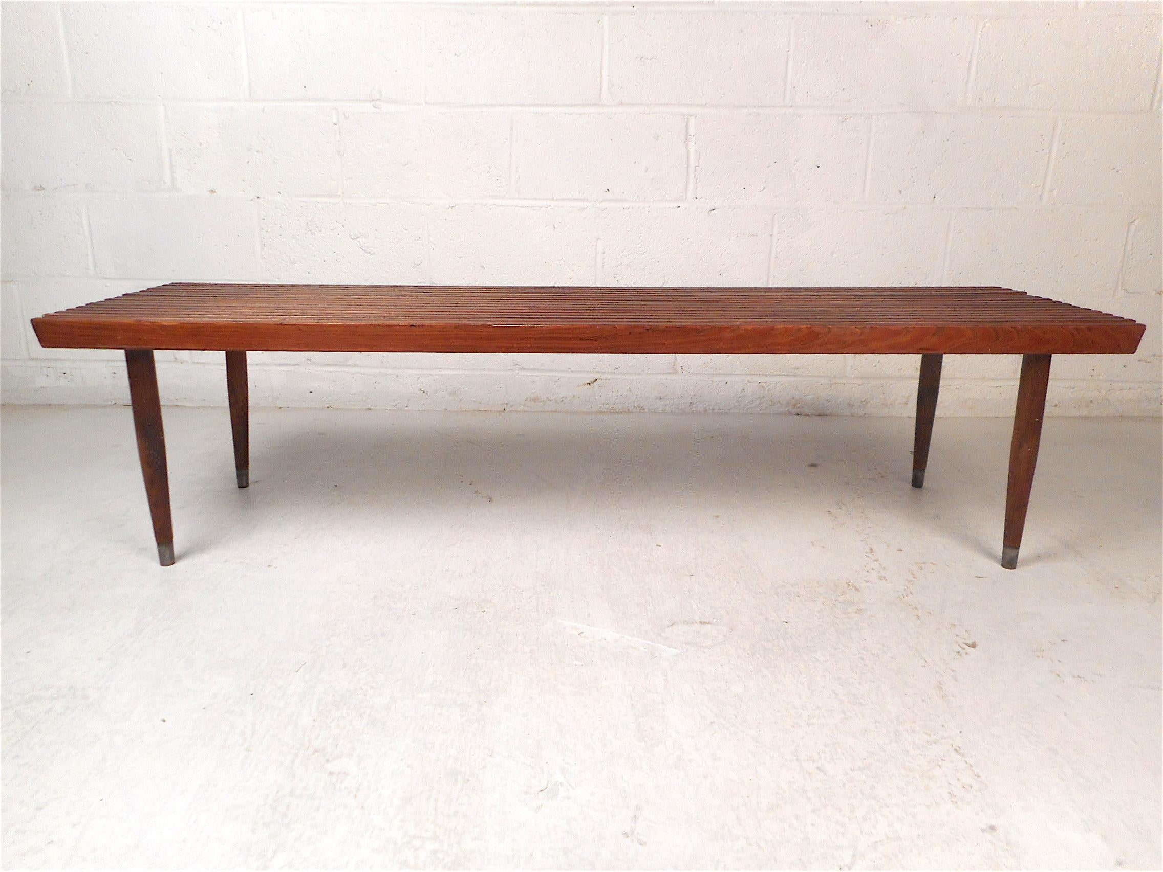 Stylish midcentury bench with a wood slat construction. Versatile design able to use for seating or as a coffee table. Nice design including tapered legs with brass sabots on their feet. Great addition to any modern interior (NJ or NY).