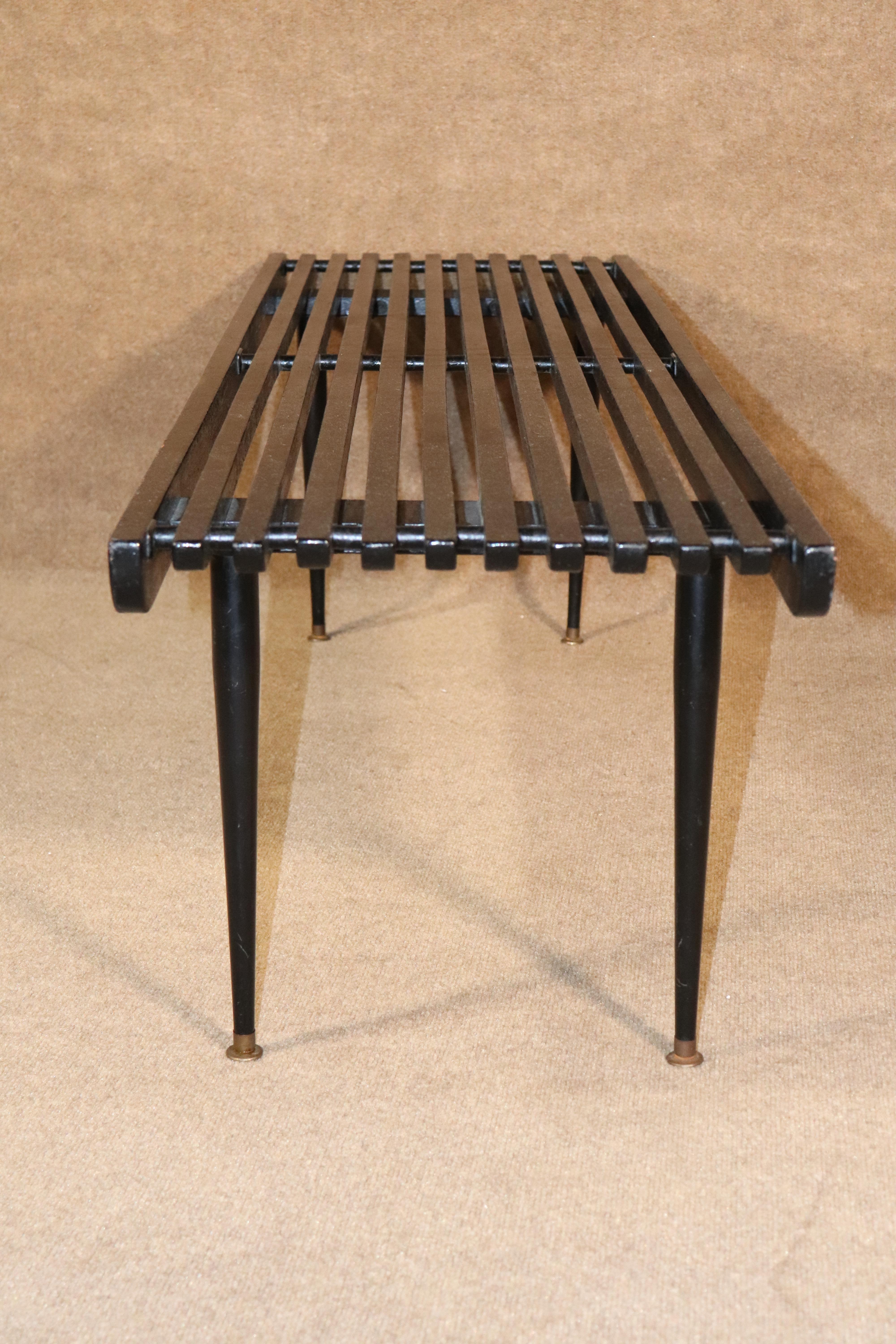Mid-Century Modern slat bench or coffee table in black. Tapered legs with brass caps.
Please confirm location.