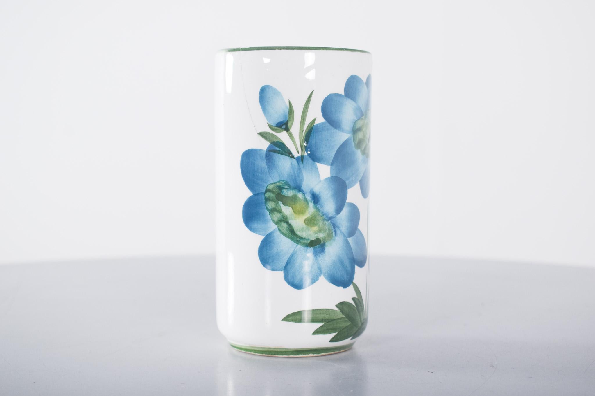 Small ceramic vase. Decorated in blue and green on white, with large vibrant blue flowers with open petals and green details on the stems and leaves, it creates a harmonious and naturalistic visual effect. The rim of the vase is gently emphasised