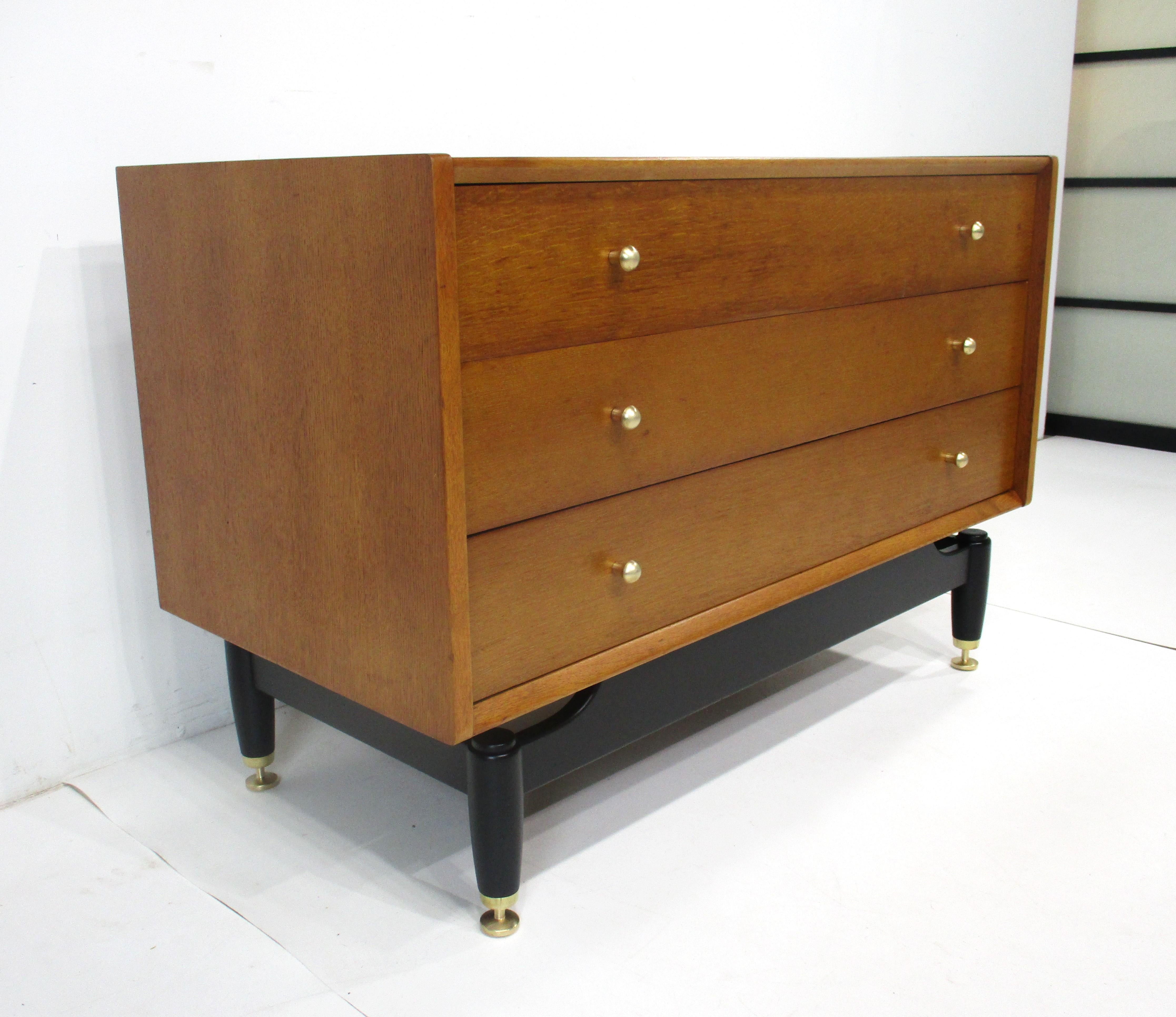 Une commode en bois à trois tiroirs de belle taille avec une base découpée en noir satiné donnant à la pièce un léger effet de flottement. Le tiroir supérieur est doté de séparateurs et de tirettes en laiton sur la face avant, ainsi que de pieds en