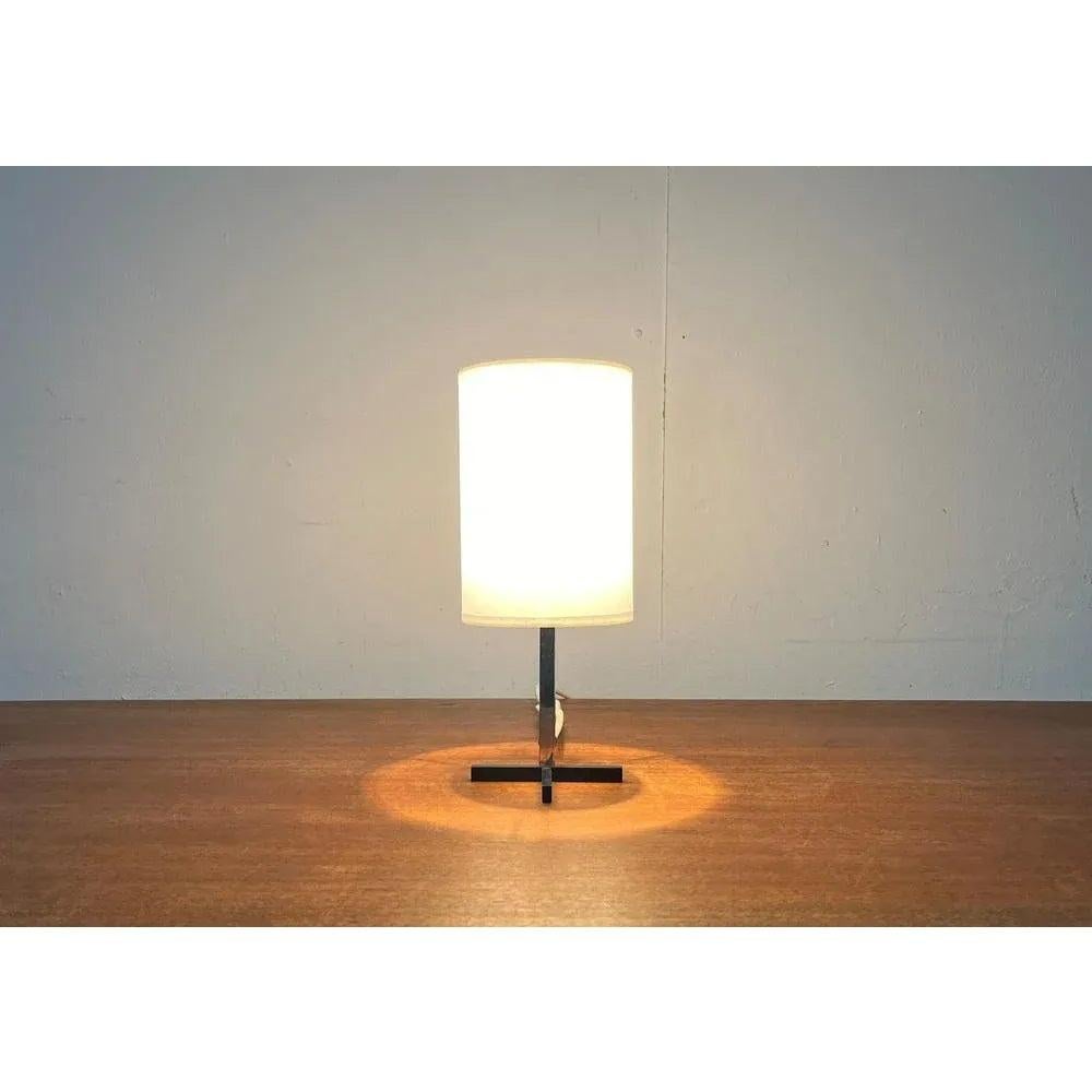 Pequeña lámpara de mesa de mediados de siglo con un pie especial.

Un diseño minimalista. Llama la atención el sencillo pie de barrotes cuadrados pintados de negro. El paraguas está cubierto de pergamino blanco. La lámpara está en muy buen estado,