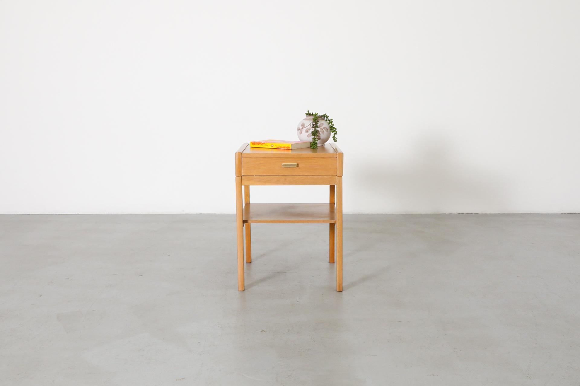 Small Mid-Century nightstand with in oak with a lower shelf and one drawer with baby blue bottom and gold toned hand pull. In original condition with wear consistent with its age and use.