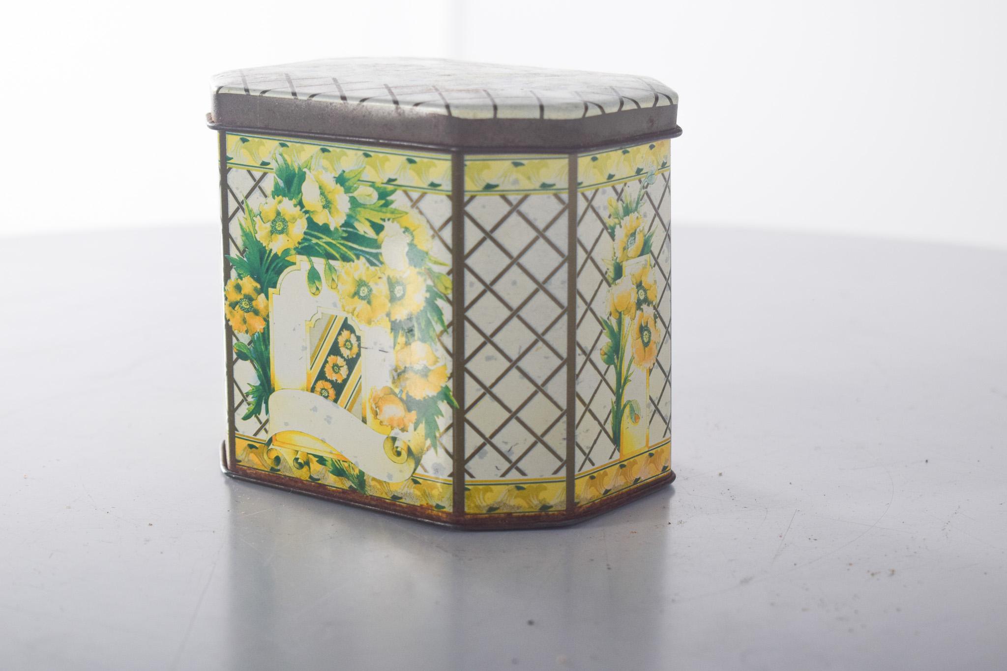 Petite boîte octogonale, en laiton. Décoration polychrome, avec un fond en damier dans des tons doux, avec des illustrations de fleurs jaunes et blanches, qui confèrent à la pièce un charme vintage et romantique. Les côtés présentent des éléments