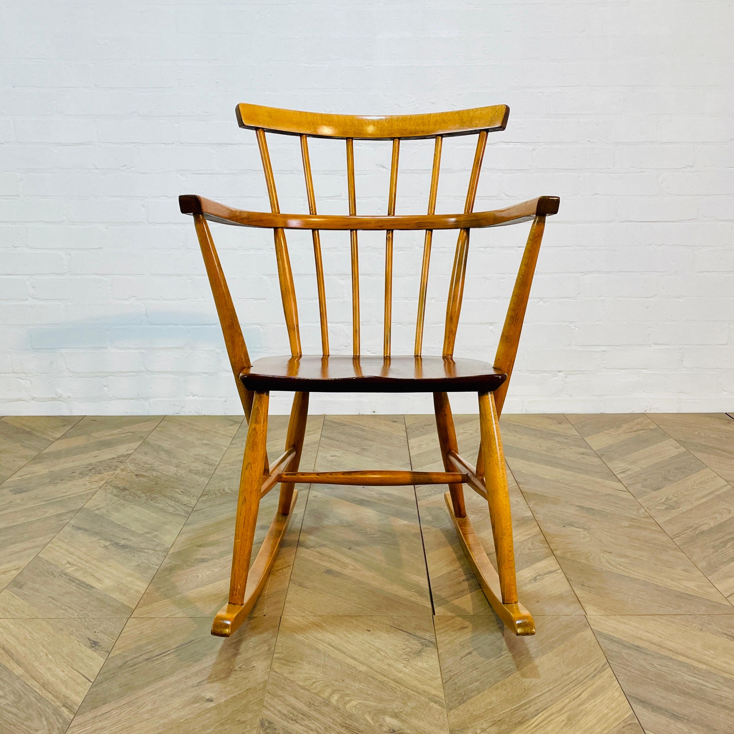 Magnifique fauteuil à bascule à dossier en fuseau bien proportionné, vers les années 1960.

La chaise, fabriquée en hêtre et en orme, est solide dans sa construction et en bon état dans l'ensemble, avec seulement des éraflures et des marques liées à