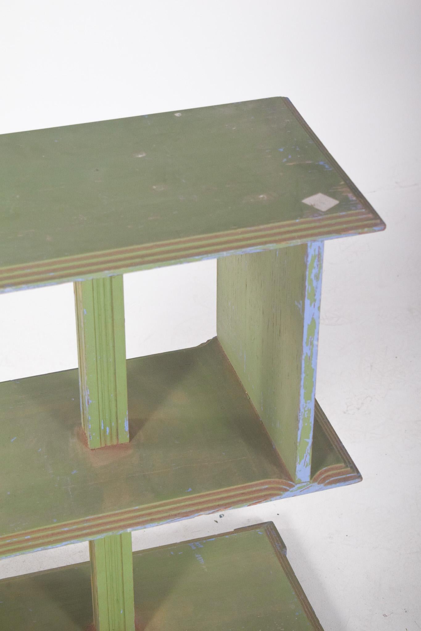 Petite bibliothèque à trois étagères. Les étagères sont disposées de manière asymétrique, reliées par des colonnes centrales verticales. La peinture verte à la finition usée révèle des couches de couleur bleue, ce qui lui confère un aspect rustique