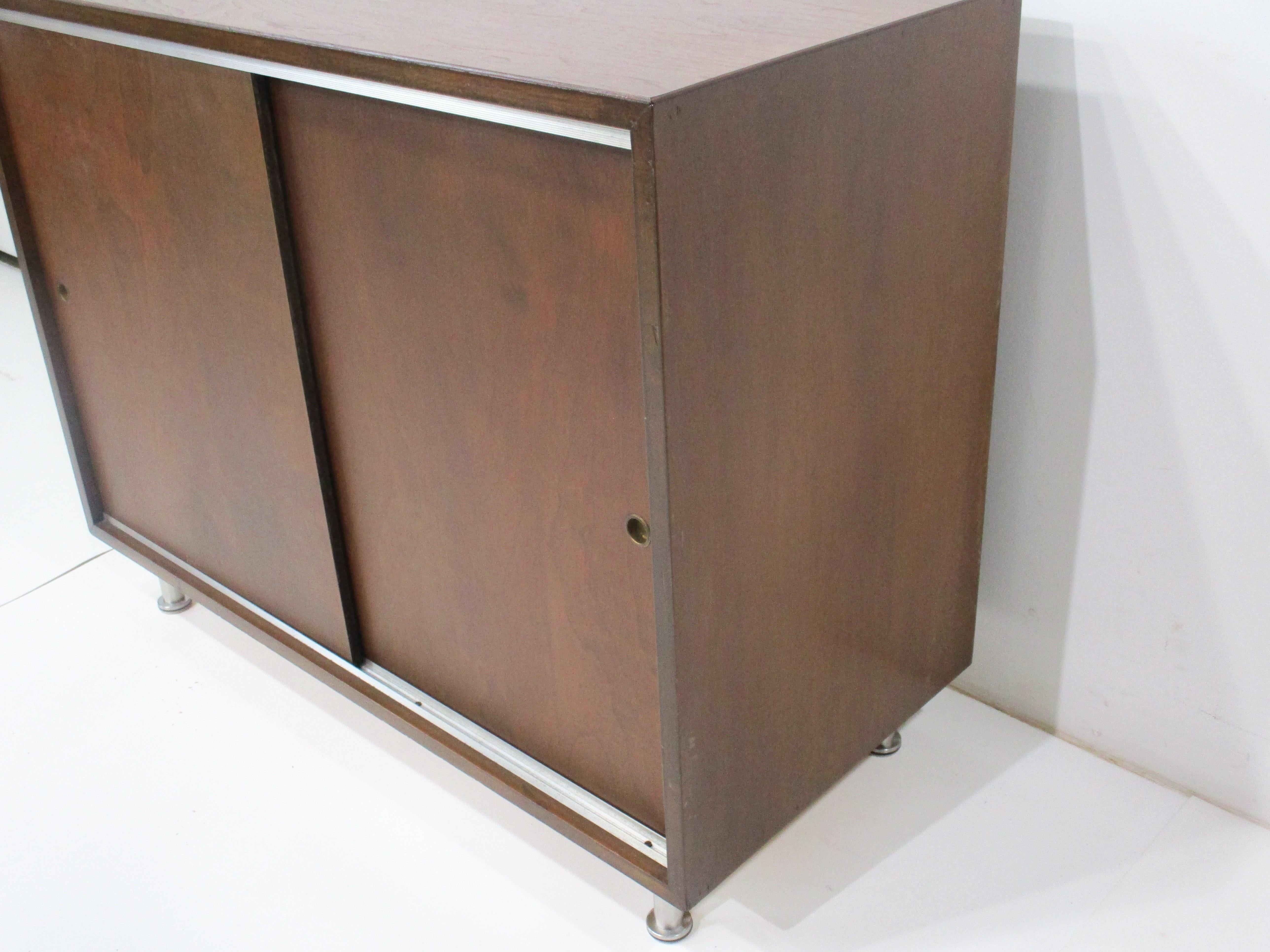 A smaller scaled walnut credenza with double sliding doors and inside one long adjustable shelve . The details of ribbed aluminum strips to the top and bottom edge and brushed aluminum legs give the piece that extra pop . Great for a thigh space or