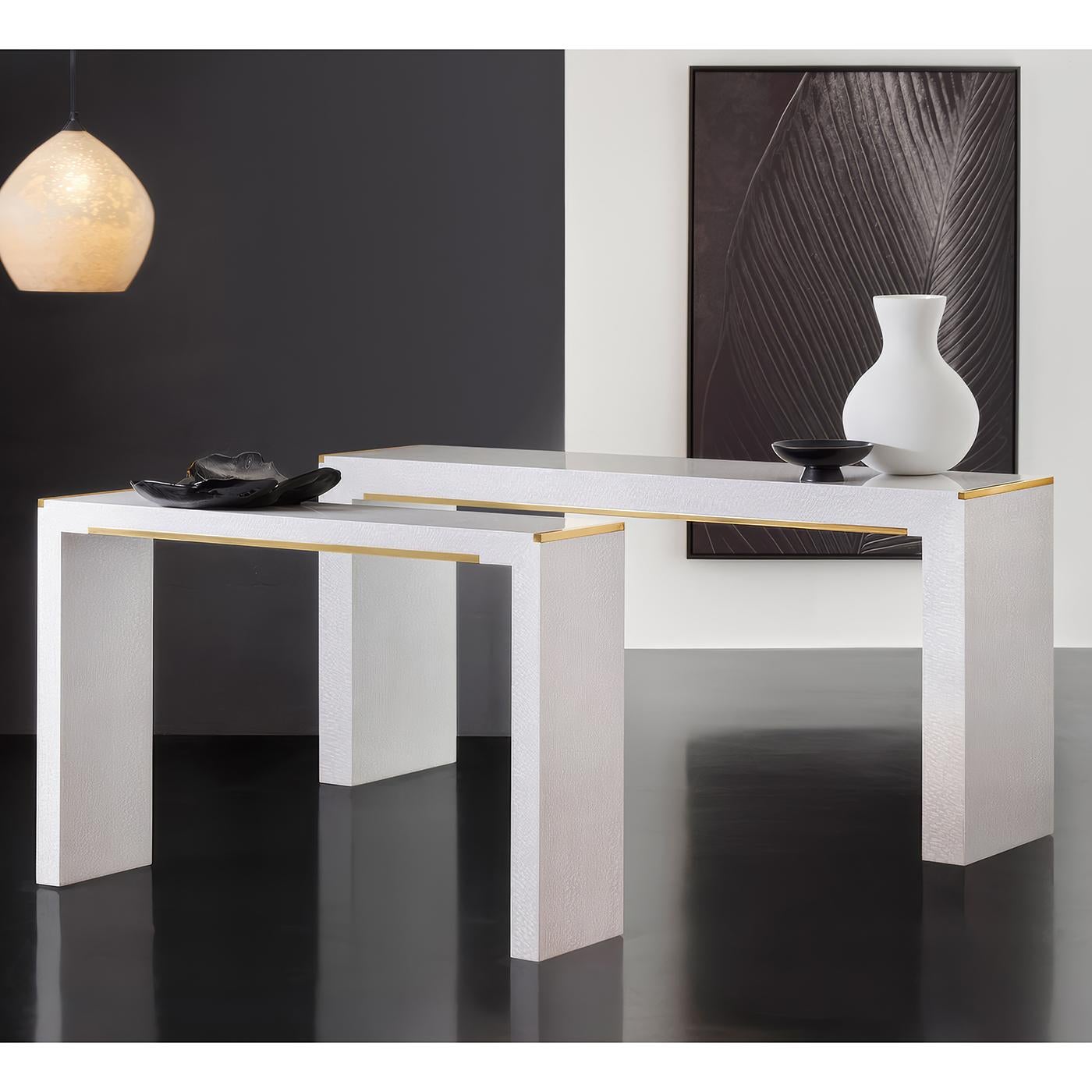 Clean modernist lines with luxurious details, featuring textured lacewood veneer in a crisp white finish. The minimalist design is enhanced by sleek brass trim along the top edge and a subtle brass crossbar detail, providing elegant metallic