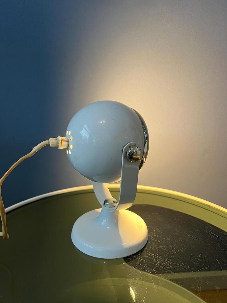 Lampe de table WHITE/SPACE Iconique avec abat-jour en forme de globe oculaire. L'abat-jour du globe oculaire peut être tourné dans n'importe quelle direction souhaitable. La pièce est en métal. La lampe nécessite une ampoule E14 et dispose