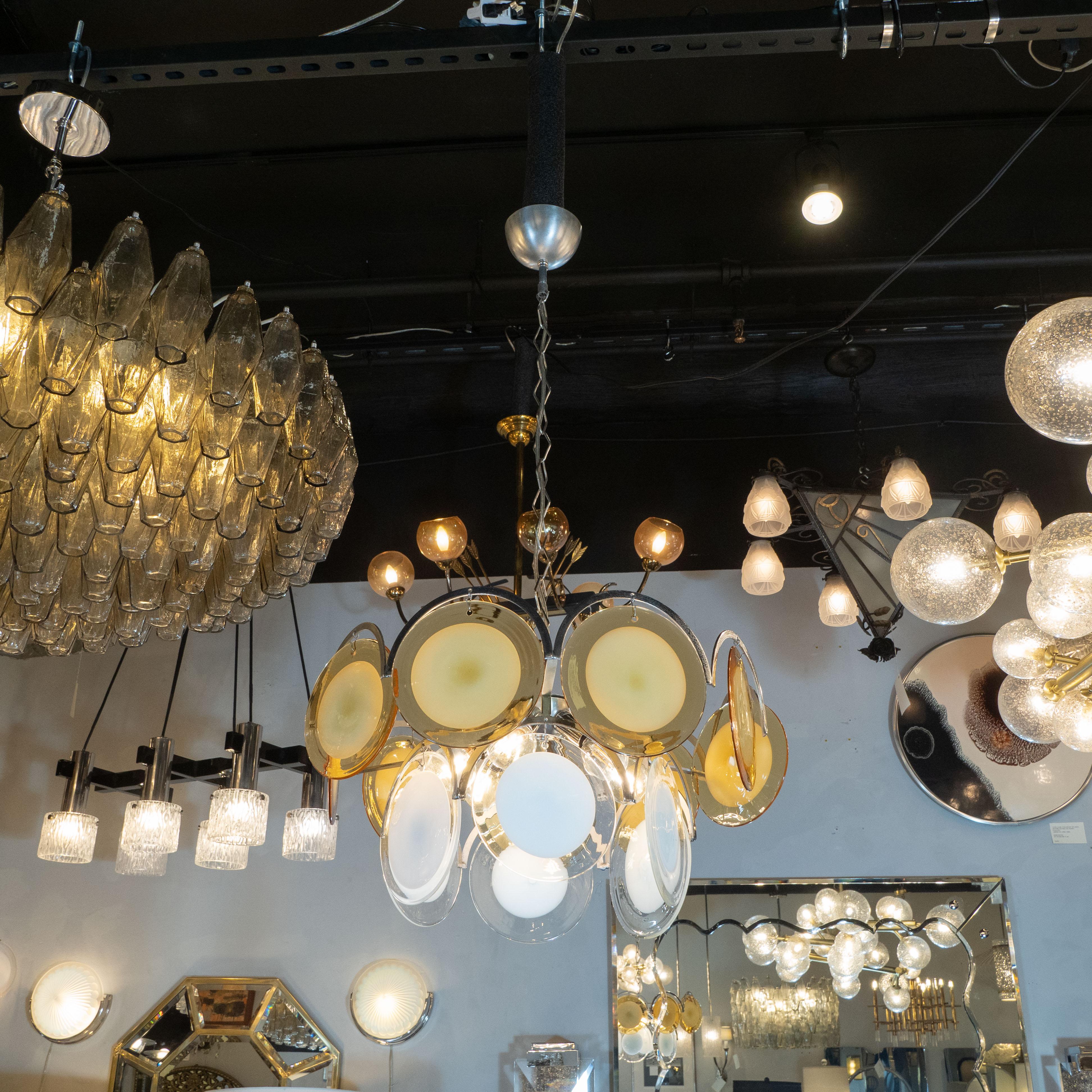 This sophisticated Mid-Century Modern chandelier attributed to Vistosi, and hand blown in Murano, Italy circa 1970. It features two tiers of glass discs, suspended from a handcrafted aluminum frame that includes demilune embellishments that trace