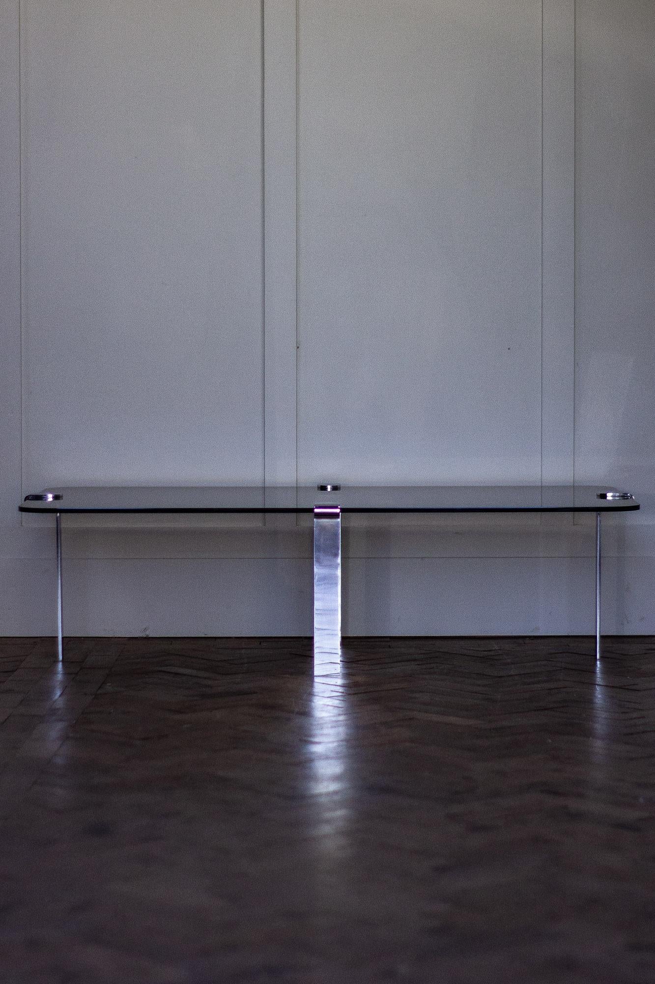 1970s smoked glass coffee table with chrome legs.

The legs have a cantilevered design, which then screws up to the glass from the underside. 

Possibly French. 
Measures:
Height 33 cm
Width 124 cm
Depth 65 cm.