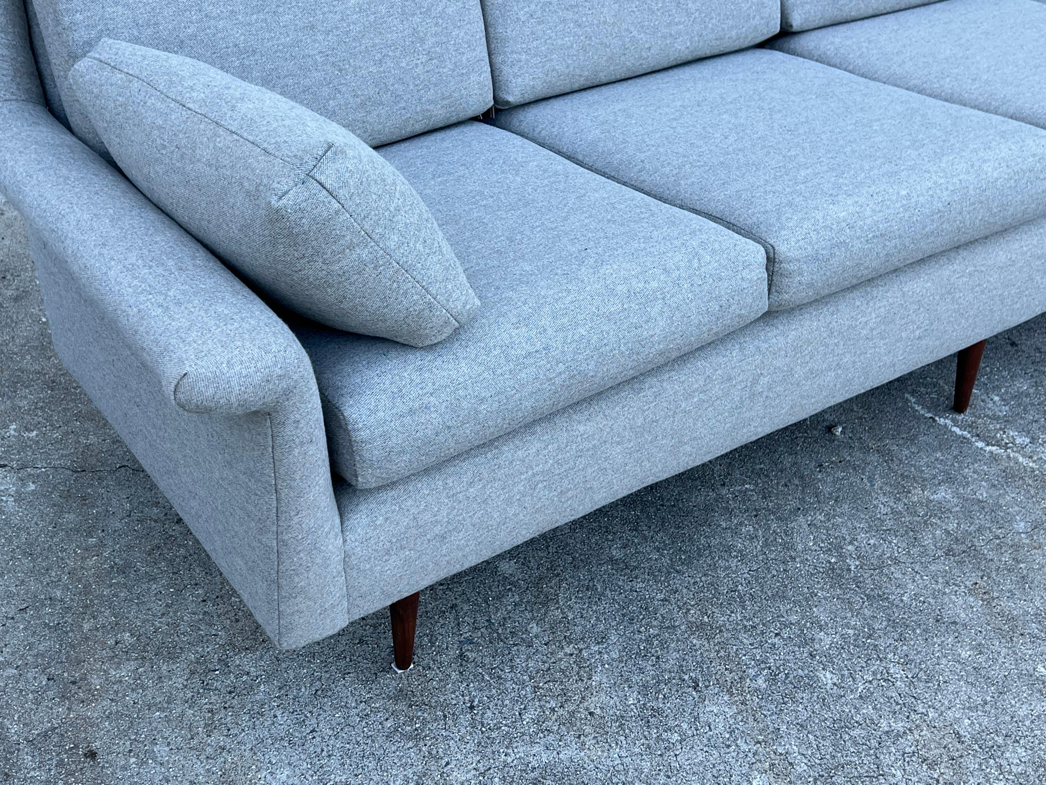 Mid-century four seater sofa designed by Milo Baughman for Thayer Coggin circa 1960s. It sits on five walnut tapered legs. We reupholstered the sofa in a wool blend fabric in a light gray color with subtle specks of blue. New foam for bottom and