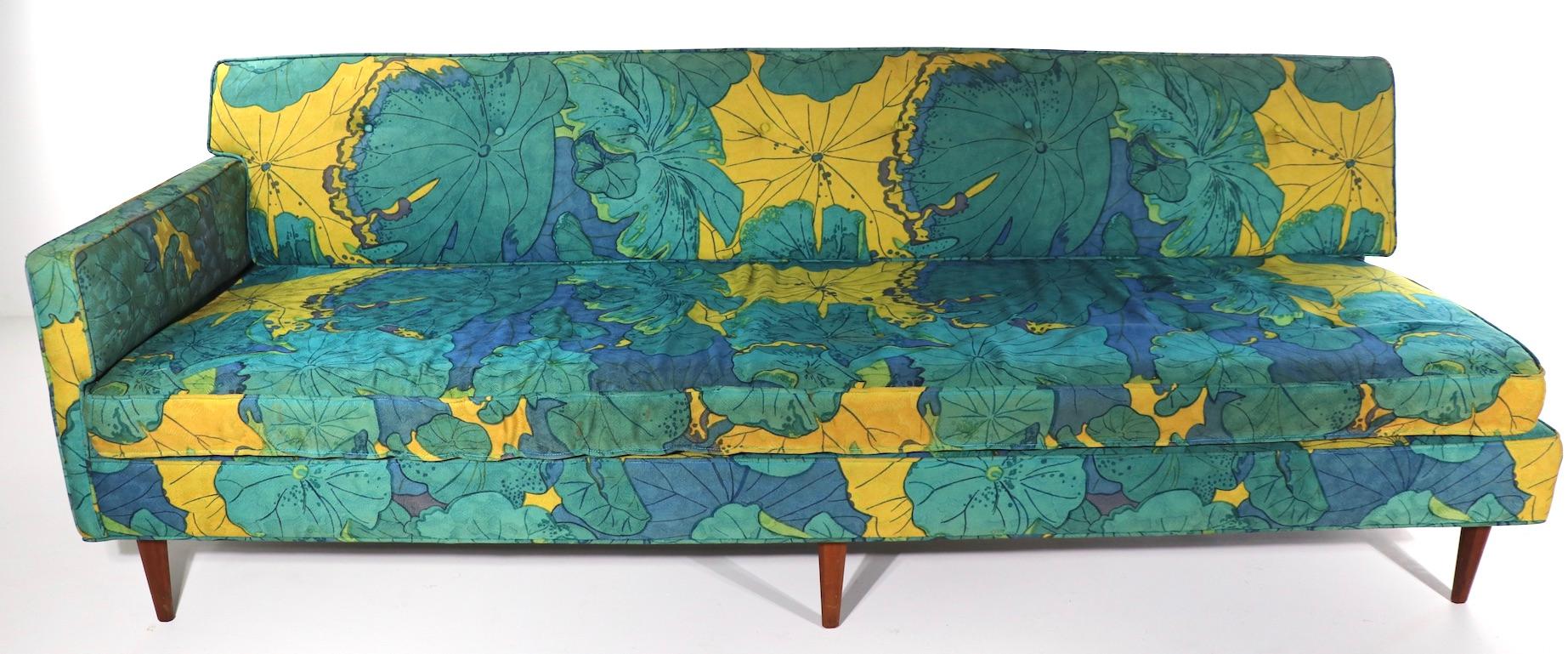 Wild exuberant foliate print mid century sofa having one side with an arm rest, and one open ended side. The fabric is still usable, but does show signs of wear, normal and consistent with age and use. We offer reupholstery services if you want a
