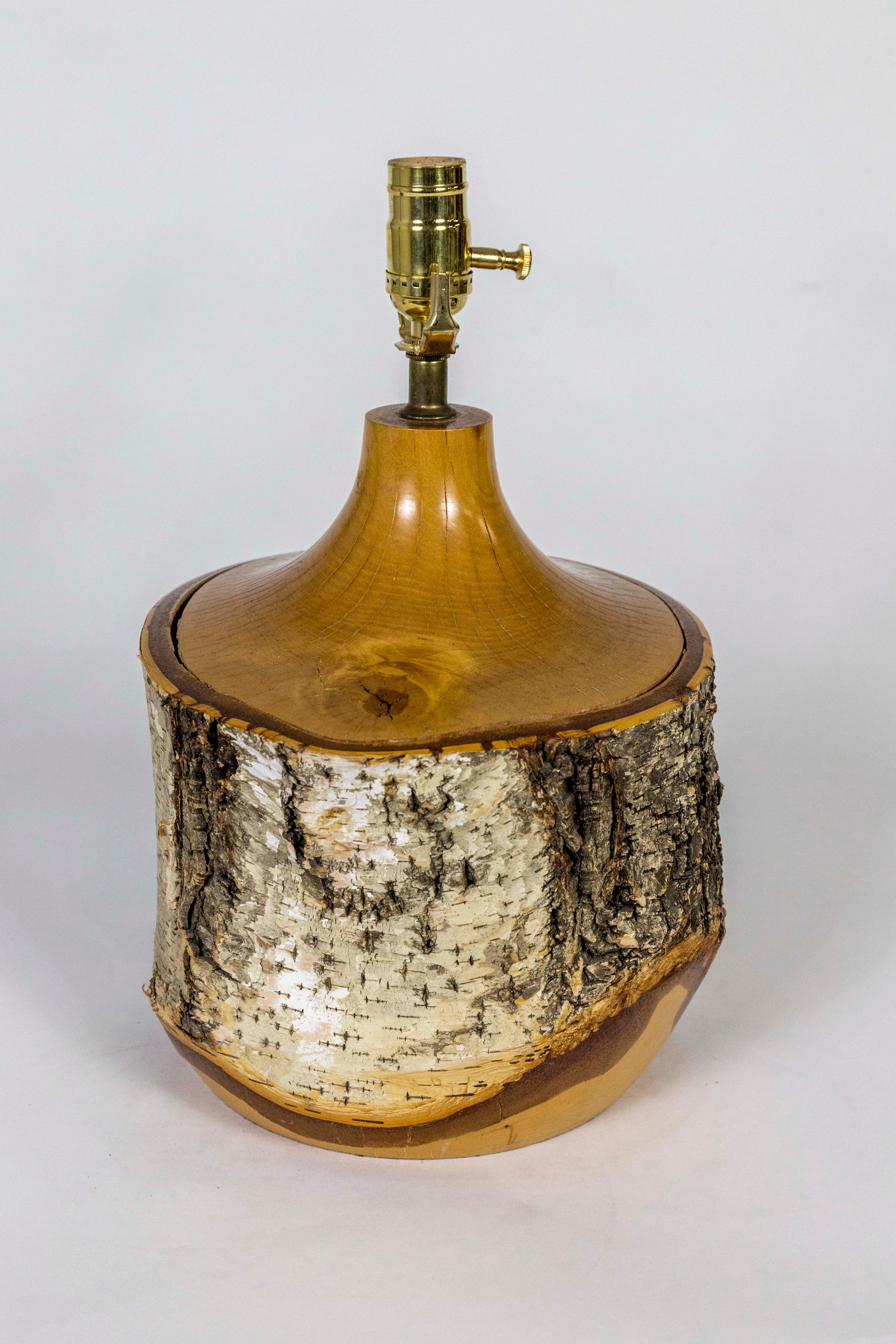 A Mid-Century Modern table lamp made from a Birch tree trunk; with sealed, intact bark. Hand-turned to create a sloping neck and rounded bottom that reveals added dimension and a golden inside color. With a shapely, hand-turned birch finial for the