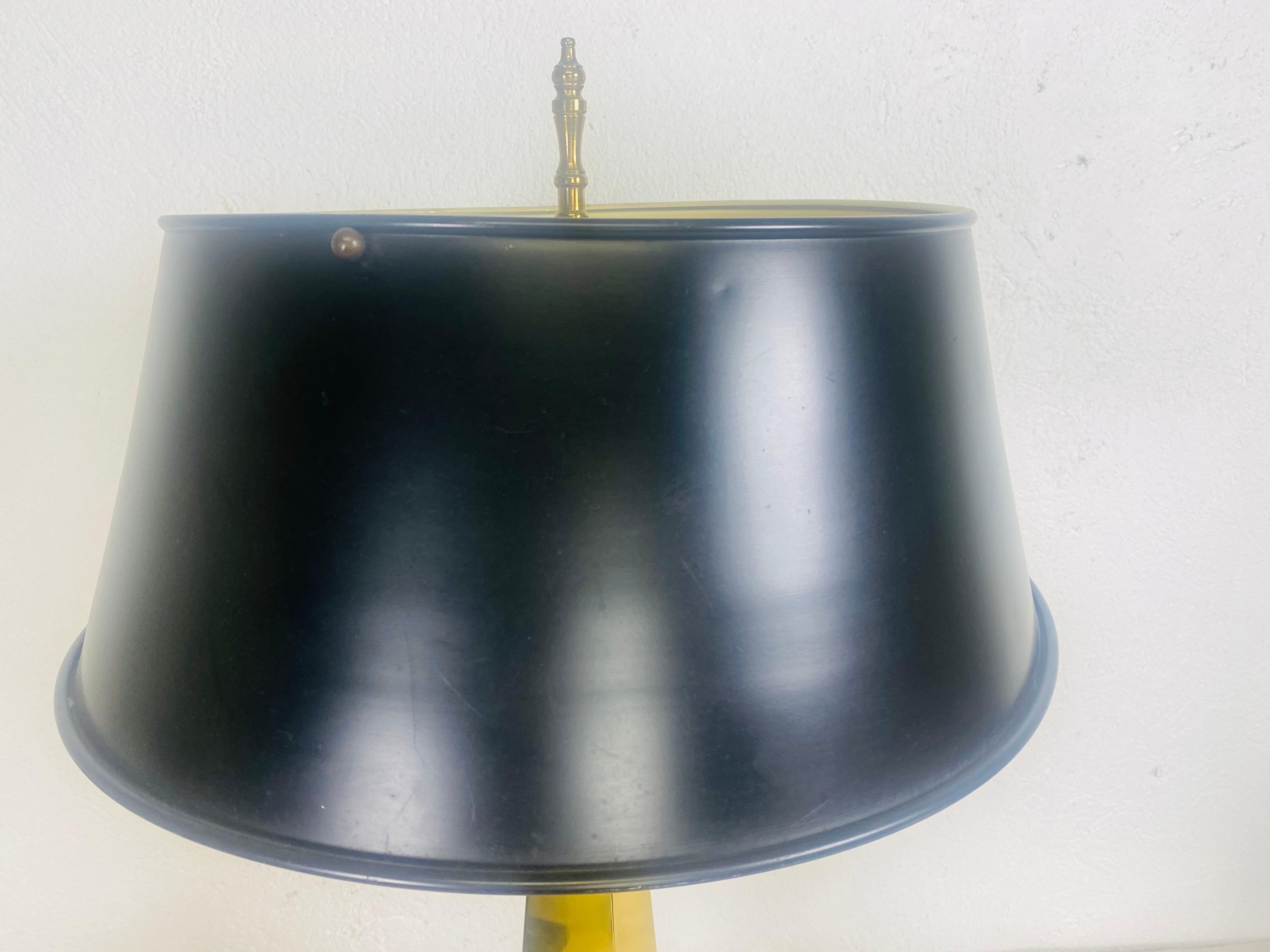 This is a handsome mid-century vintage library style solid brass obelisk lamp. This obelisk lamp has a pedestal with four ball feet, holding up the obelisk with a metal black lacquered lampshade. This obelisk lamp is in the manner of Chapman circa