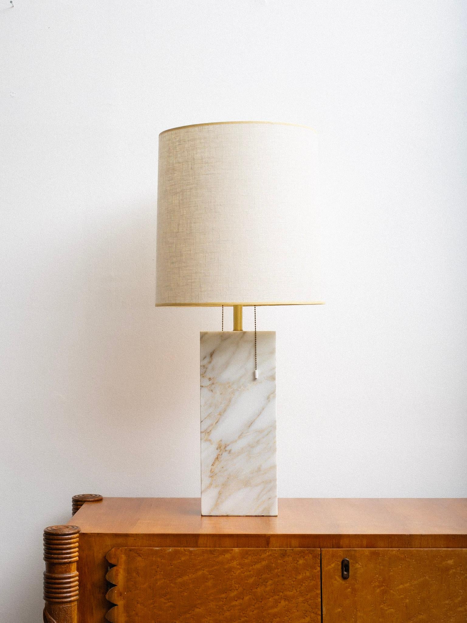 Mid century marble table lamp in the style of Nessen Studios. Rectangular solid marble with natural veining in cream and beige tones. Features a brass-finished central column with dual bulb sockets and pull-chain switches. Heavy in weight. Shade not