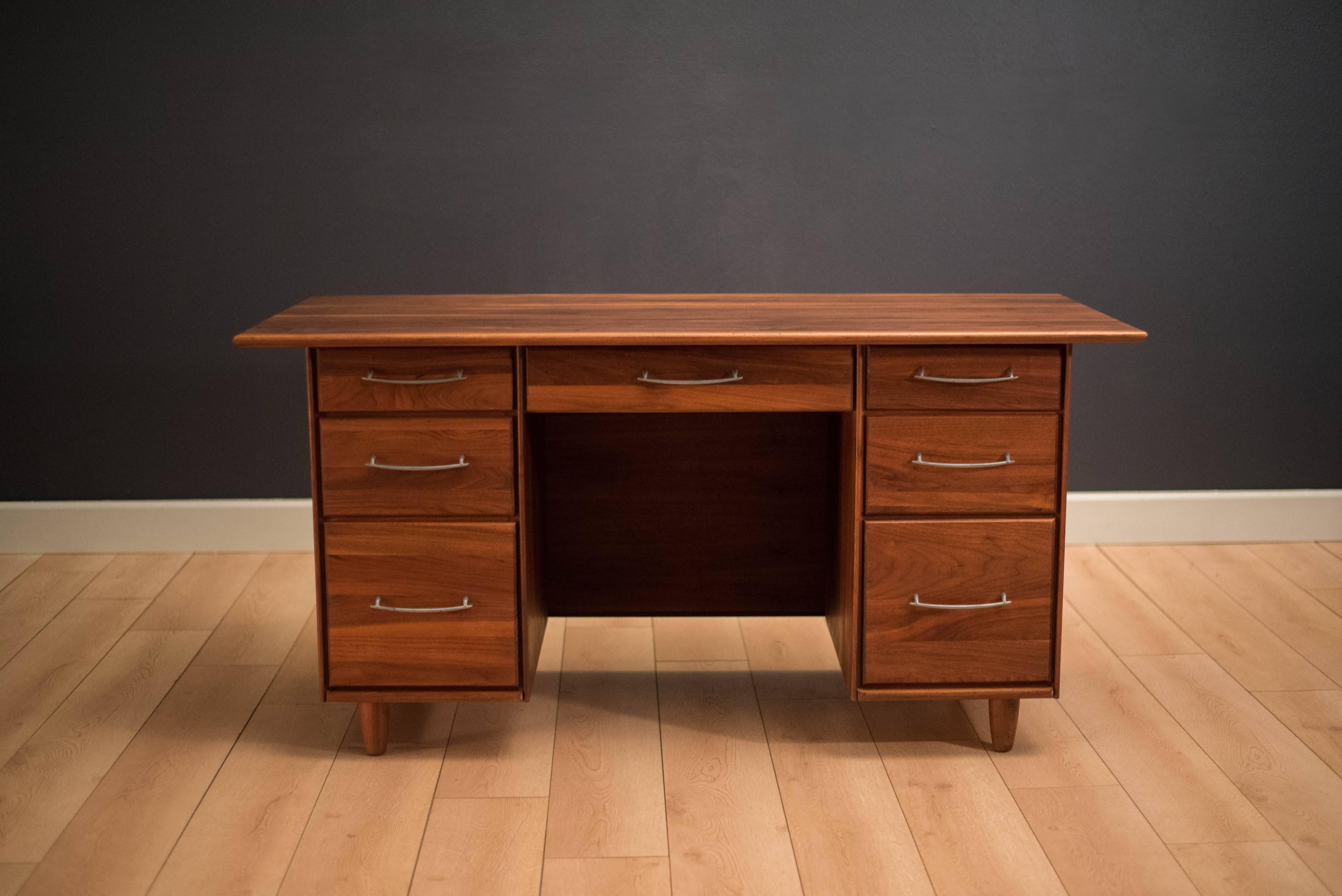 Mid-Century Modern prelude desk for ACE-HI in solid planked walnut. This desk offers plenty of storage space complete with seven spacious drawers accessorized with pewter handles. Finished on the back and can be displayed from any angle.
 