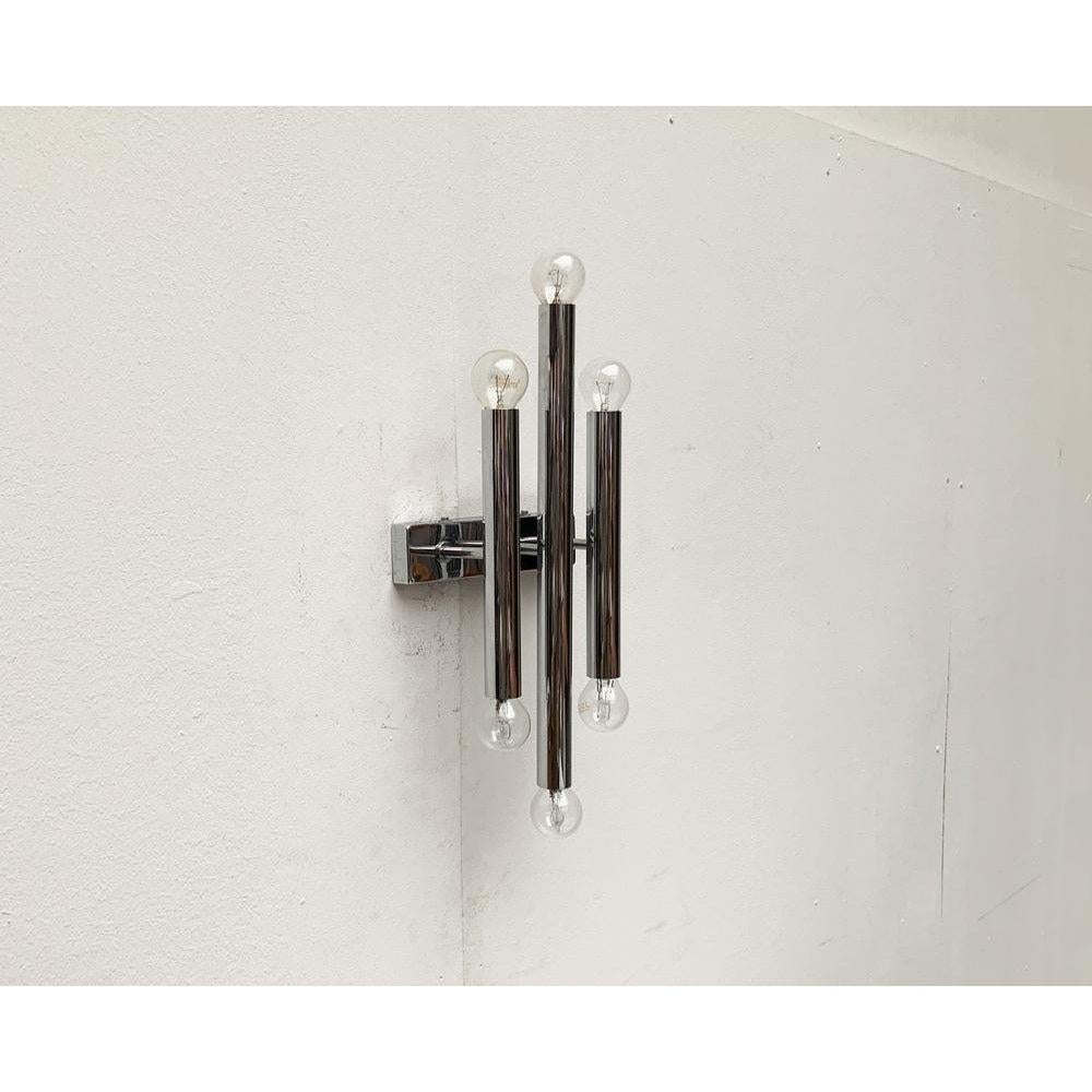 Imponente lampada da parete in cromo.

Un design senza tempo che convince per la sua geometria semplice e accurata. Tre cilindri paralleli con le estremità superiore e inferiore che si appoggiano su calzini. I cilindri sono montati con delle