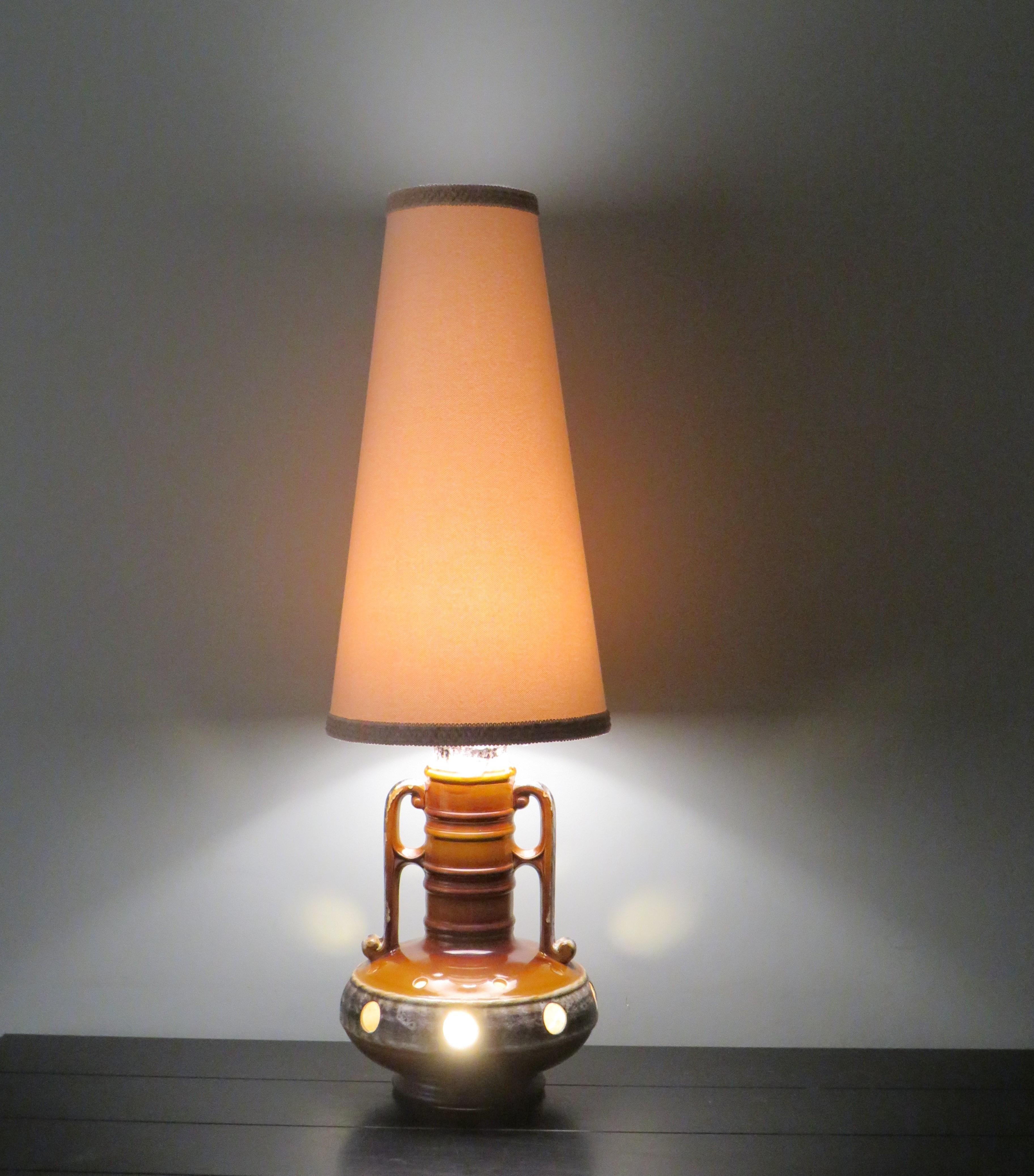 Grand lampadaire en céramique de lave grasse de couleur caramel avec des accents beiges et bruns.
La lampe a un abat-jour beige clair avec une bordure en bas et en haut dans les mêmes tons que l'abat-jour.
La base de la lampe comporte 2 points