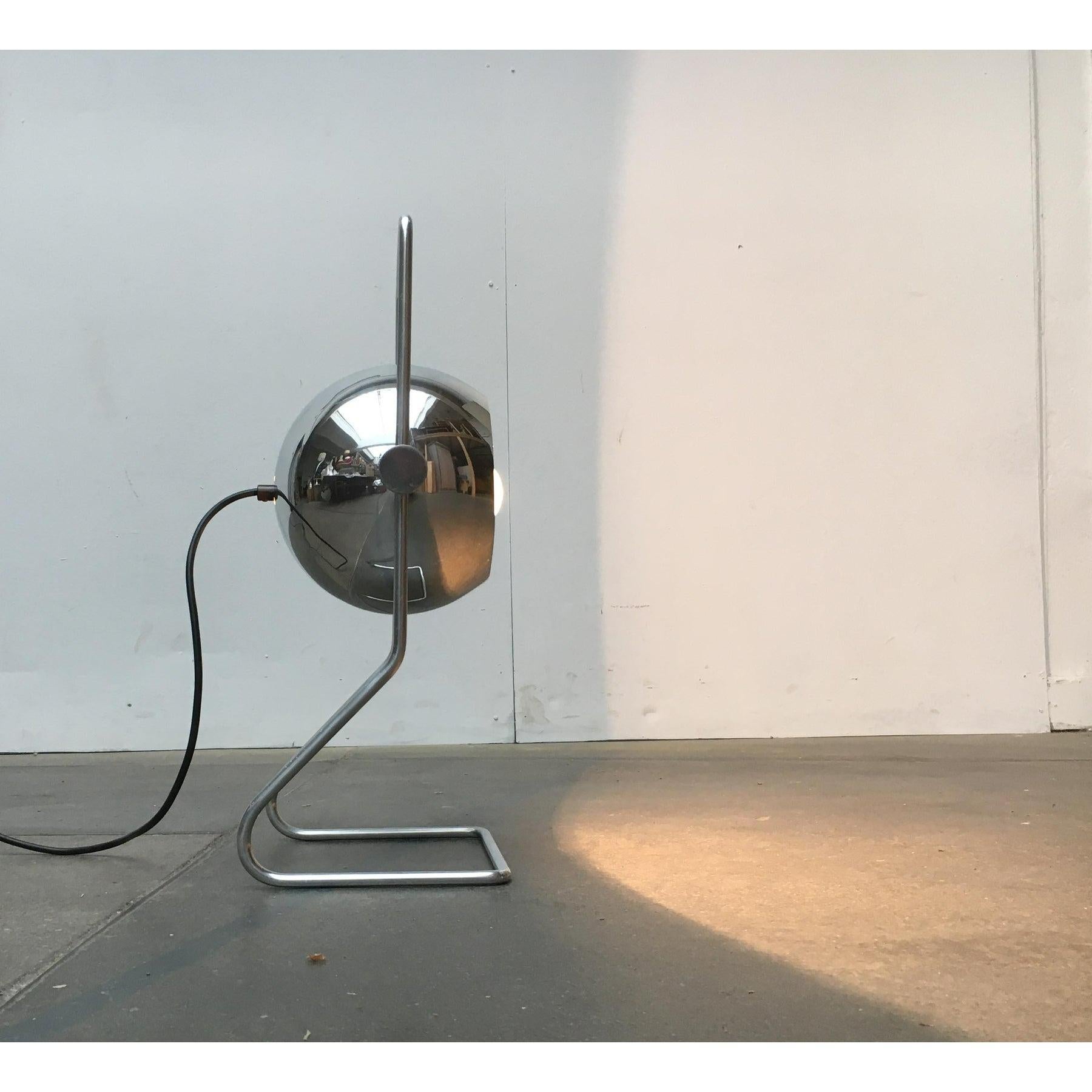 Space Age floor lamp.

A functional design. A movable sphere is suspended in a frame. The frame consists of a continuous aluminum rod. It forms a base at the bottom and a handle at the top. The reflector ball is fixed in the frame in an inclinable
