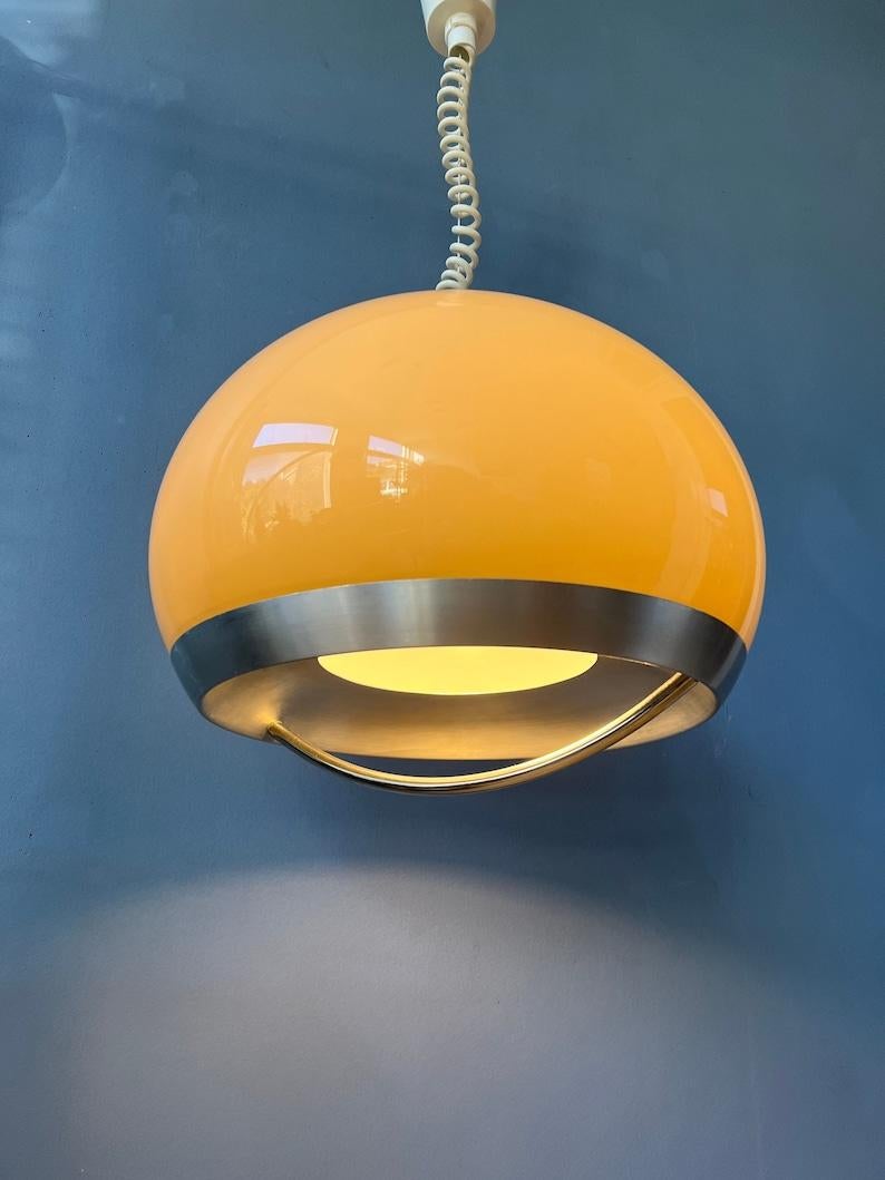 Beautiful space age pendant by Dijkstra in beige/mocca colour and aluminium/metal frame. The shade produces a magnificent glow, reflecting nicely on the chrome arc underneath the shade. The lamps requires an E27 (standard) lightbulb.

Additional