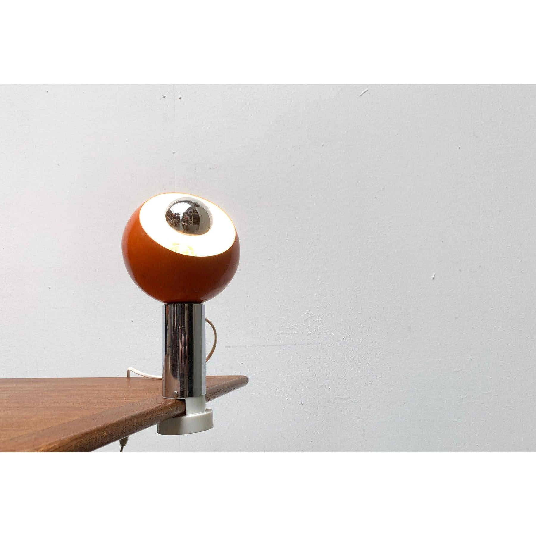 Space Age clamp lamp with spherical reflector on magnetic holder.

A striking detail of this lamp is the spherical lamp head. This is held with a magnet and can thus be flexibly aligned. The head is orange and has a white reflector inside. The