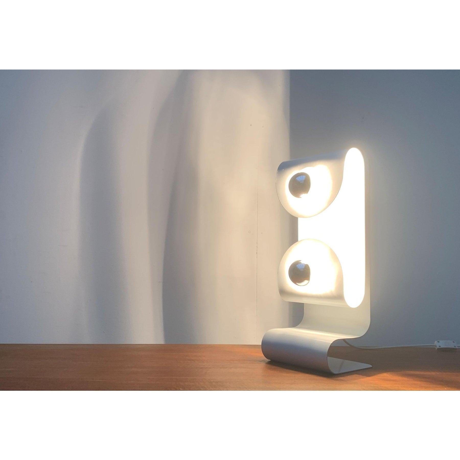 Imposante lampe de table de l'ère spatiale.

Le design est basé sur le principe du Foldes et l'ajout d'éléments concaves et convexes. Une boîte de conserve courbée et incurvée forme le pied. La tête du Luminaire est constituée d'une feuille montée
