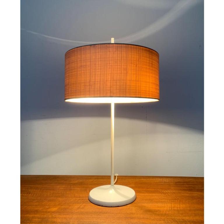 Elegante lampe de table Mid Century.

Un design avec un langage simple de la forme. Un abat-jour en forme de tambour repose sur une longue tige. L'abat-jour est fermé en haut par un disque diffuseur en acrylique translucide. La tige étroite se fond