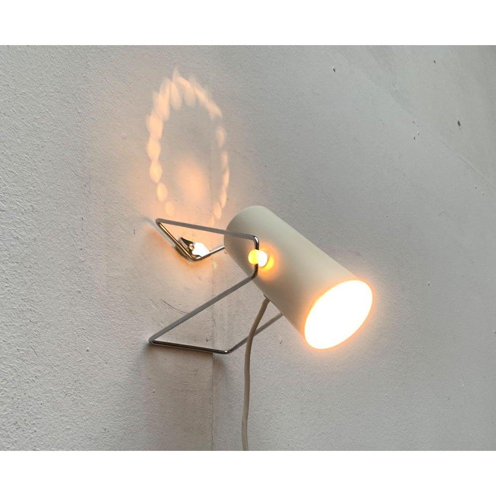 Minimalist mid century table or wall light

This little lamp looks like a lively character. The lamp head has the shape of a cylinder that widened minimally forward. The back is closed and provided with a ring -shaped perforation. The light head is