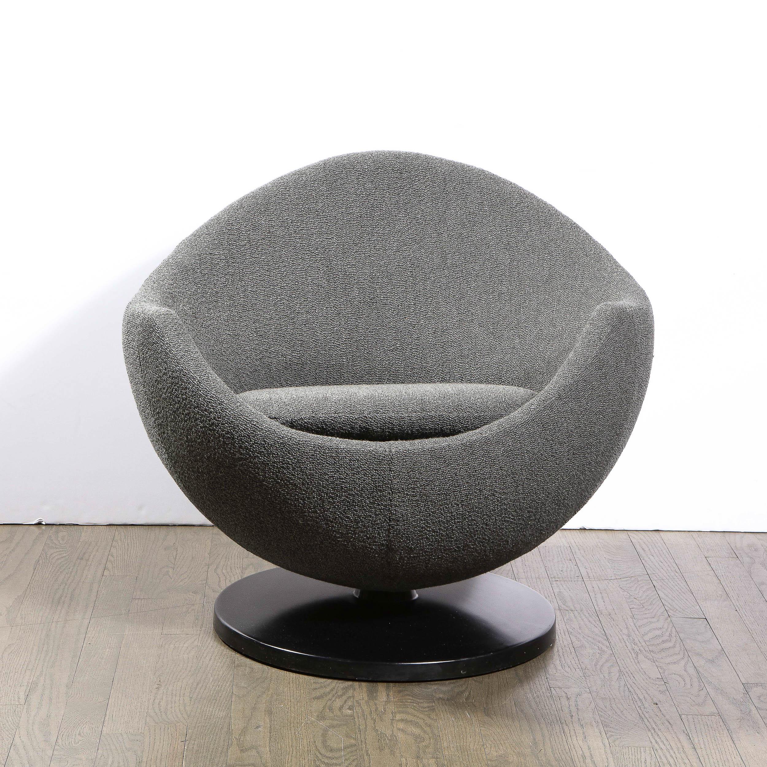 This stunning Mid-Century Modern swivel chair was realized in the United States circa 1960. Sitting on a subtly convex black enamel base, this curvilinear chair offers a graphic form with a rounded back; dramatically concave arms; and a peaked back-