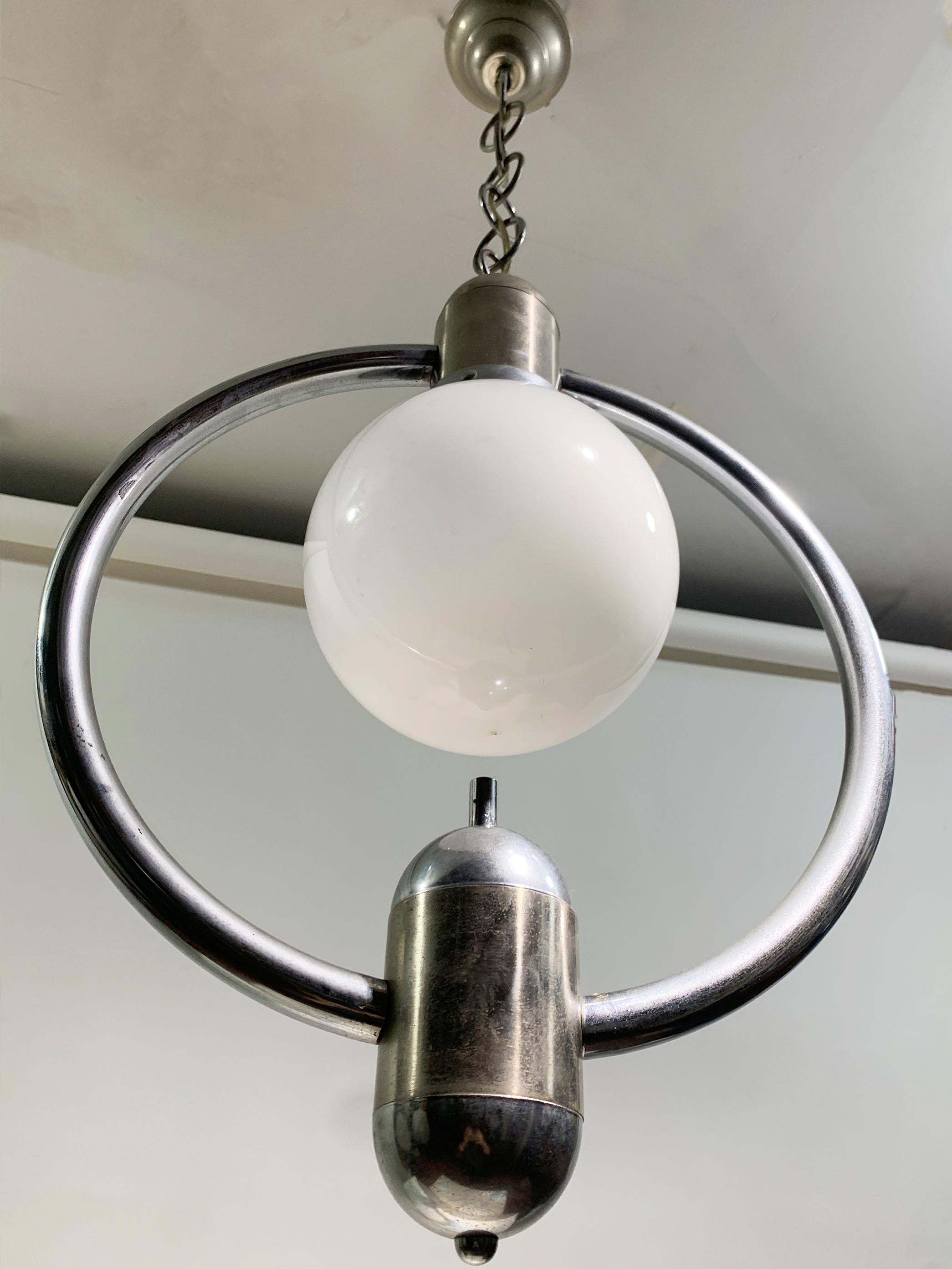 Diese Mid-Century Modern-Pendelleuchte hat einen eleganten verchromten Metallrahmen mit kreisförmiger Struktur und verkörpert eine futuristische und atomare Ästhetik. Das Herzstück ist eine kugelförmige weiße Glaskugel, die das Licht gleichmäßig