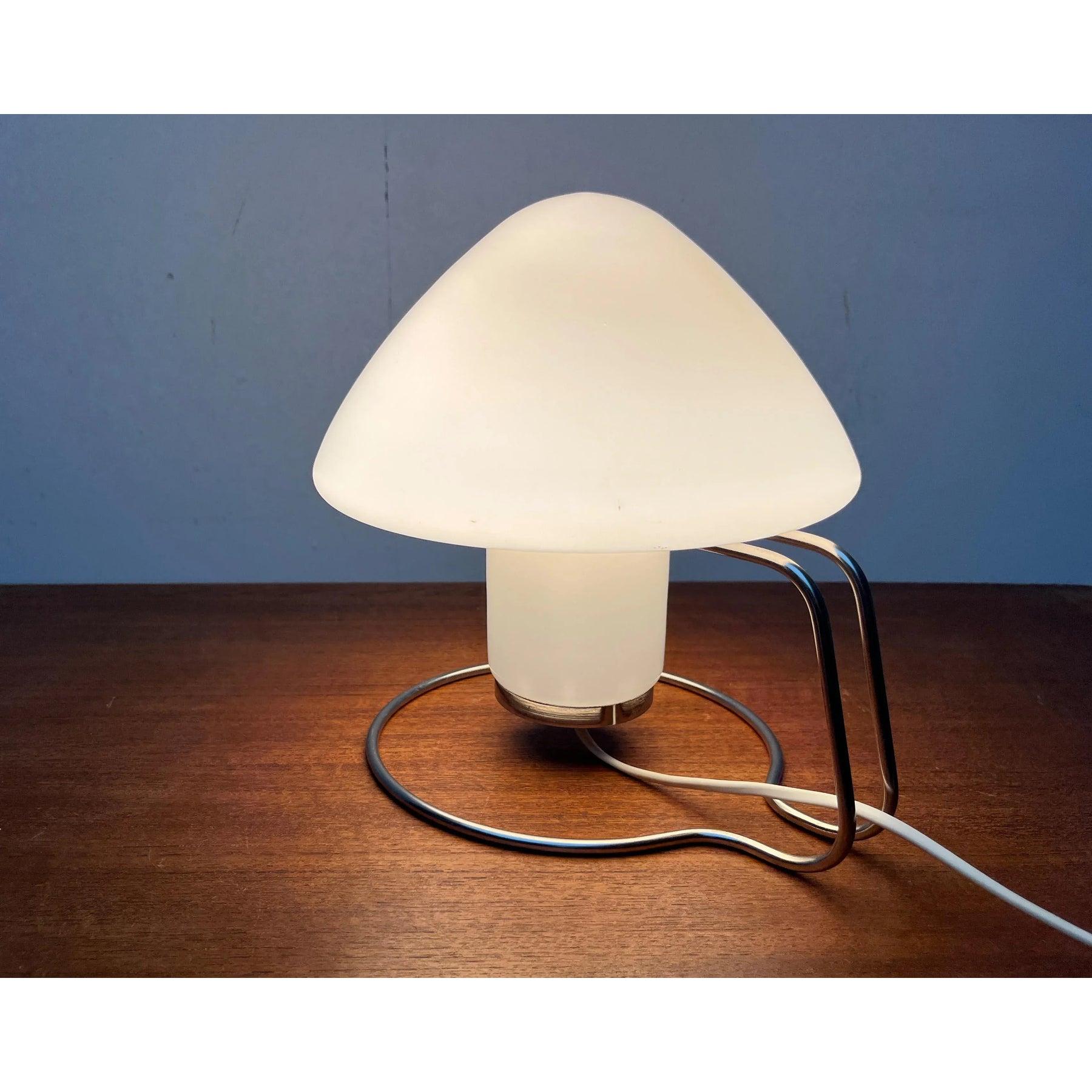 Rare lampe de table de la NO AGE avec une base remarquable.

Le verre est en forme de champignon et recouvert de blanc. Il repose librement dans un cadre métallique. Le pied est divisé en anneaux continus. L'anneau supérieur, plus petit, contient le