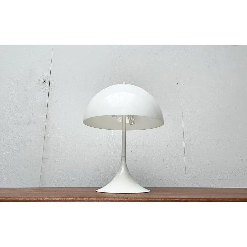Lampe de table simple dans le style Panthella de Böhmer glow.

Le corps de la lampe, entièrement blanc, se compose de deux éléments, le pied en forme de trompette et l'abat-jour caractéristique. Le parapluie hémisphérique est fabriqué en plastique