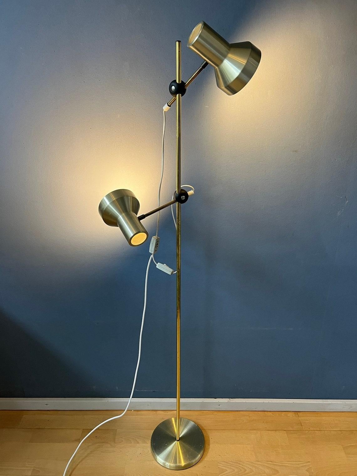 A vintage space age floor lamp with two aluminium spots in silver/gold colour.. The spots (and their arms) can be turned in any direction desirable and move up and down the base. The spots can be switched on simultaneously or separately. The lamp