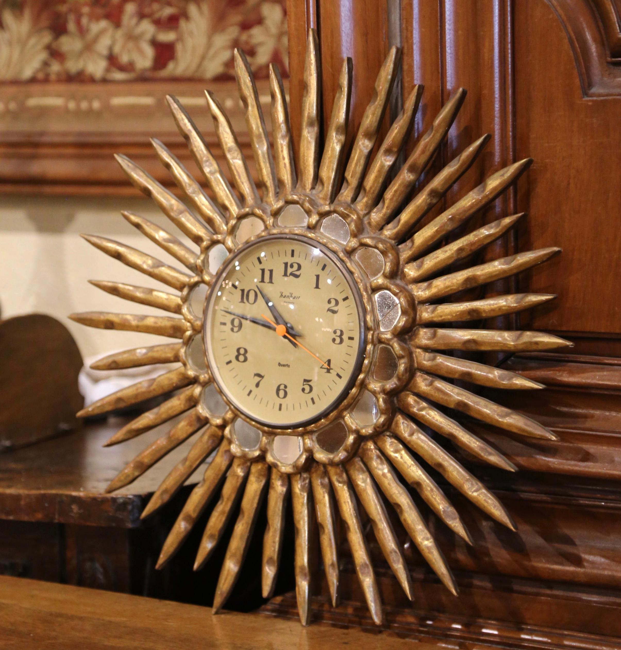 Add a touch of elegance to your home with this striking gilt wood sunburst clock, hand-carved in Spain circa 1970. This vintage piece features a central circular dial, surrounded by mirrored insets and a series of radiant, gilded rays—a design